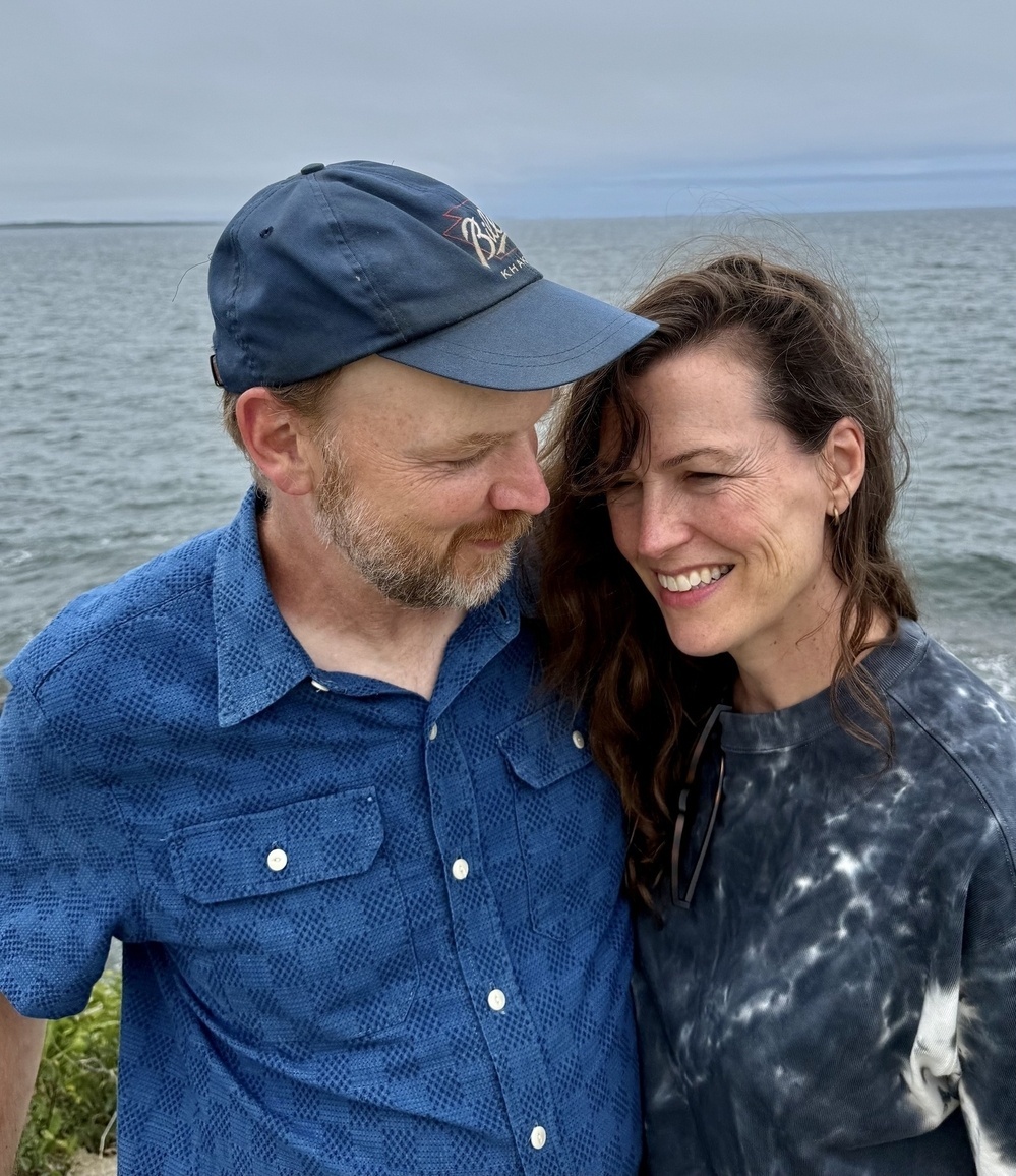 Sara and Brian standing in front of the Atlantic ocean, looking at each other.