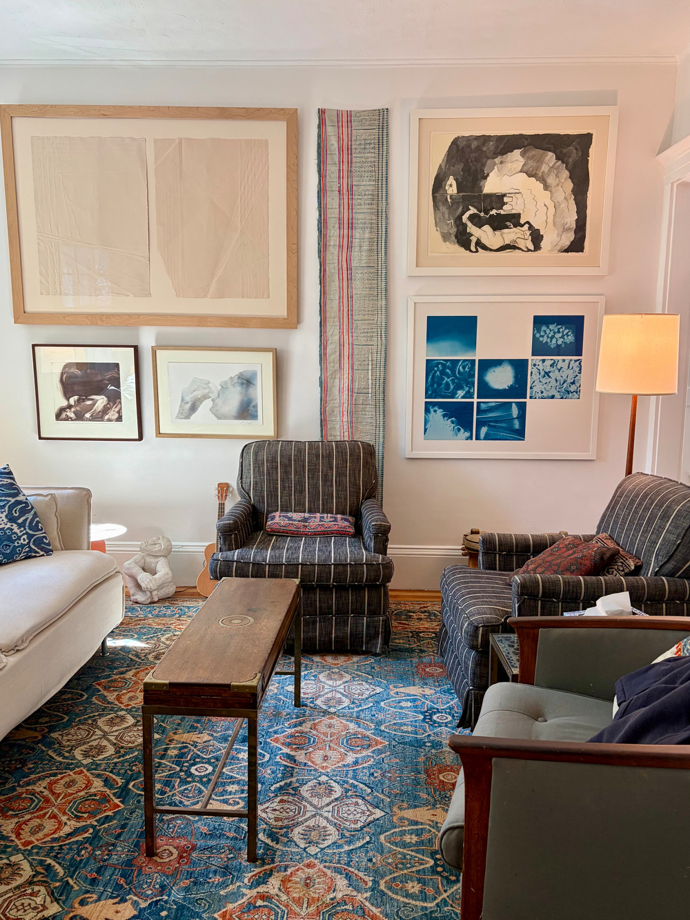That same white living room, now with floor to ceiling artworks, warm textiles and lamps.