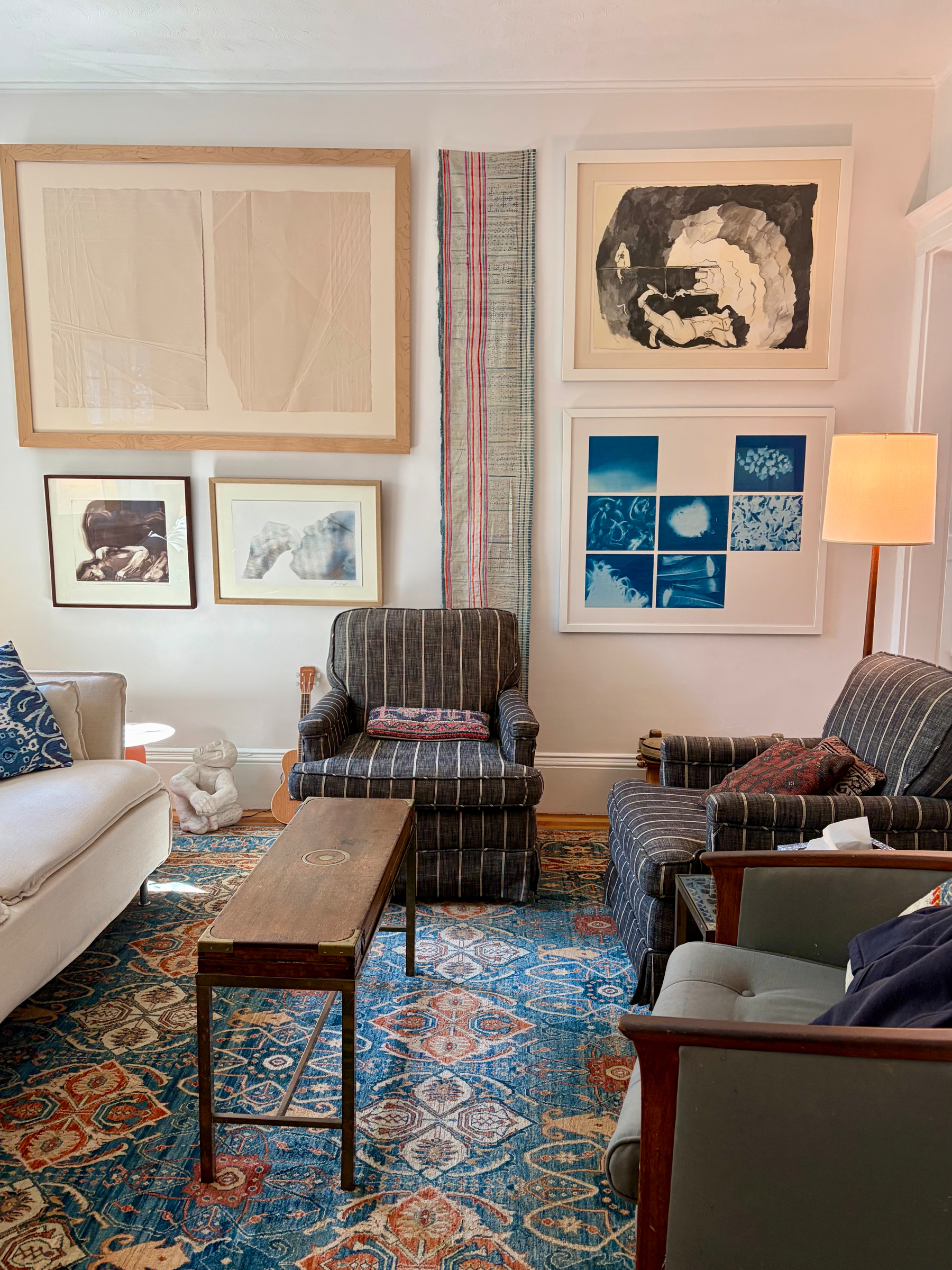That same white living room, now with floor to ceiling artworks, warm textiles and lamps. 