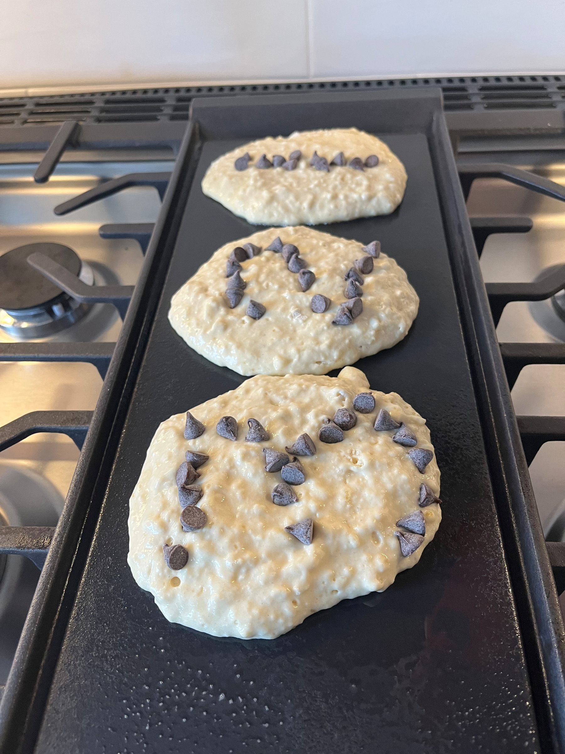 On the griddle, three pancakes feature chocolate chips in the shapes of the numbers three, two, and one, respectively 