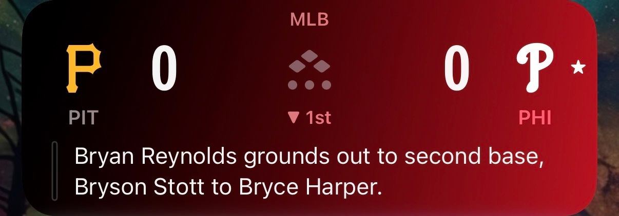 A baseball game between the Pittsburgh Pirates and Philadelphia Phillies is scoreless in the bottom of the first inning with a play where Bryan Reynolds grounds out to second base, and Bryson Stott is thrown out by Bryce Harper.