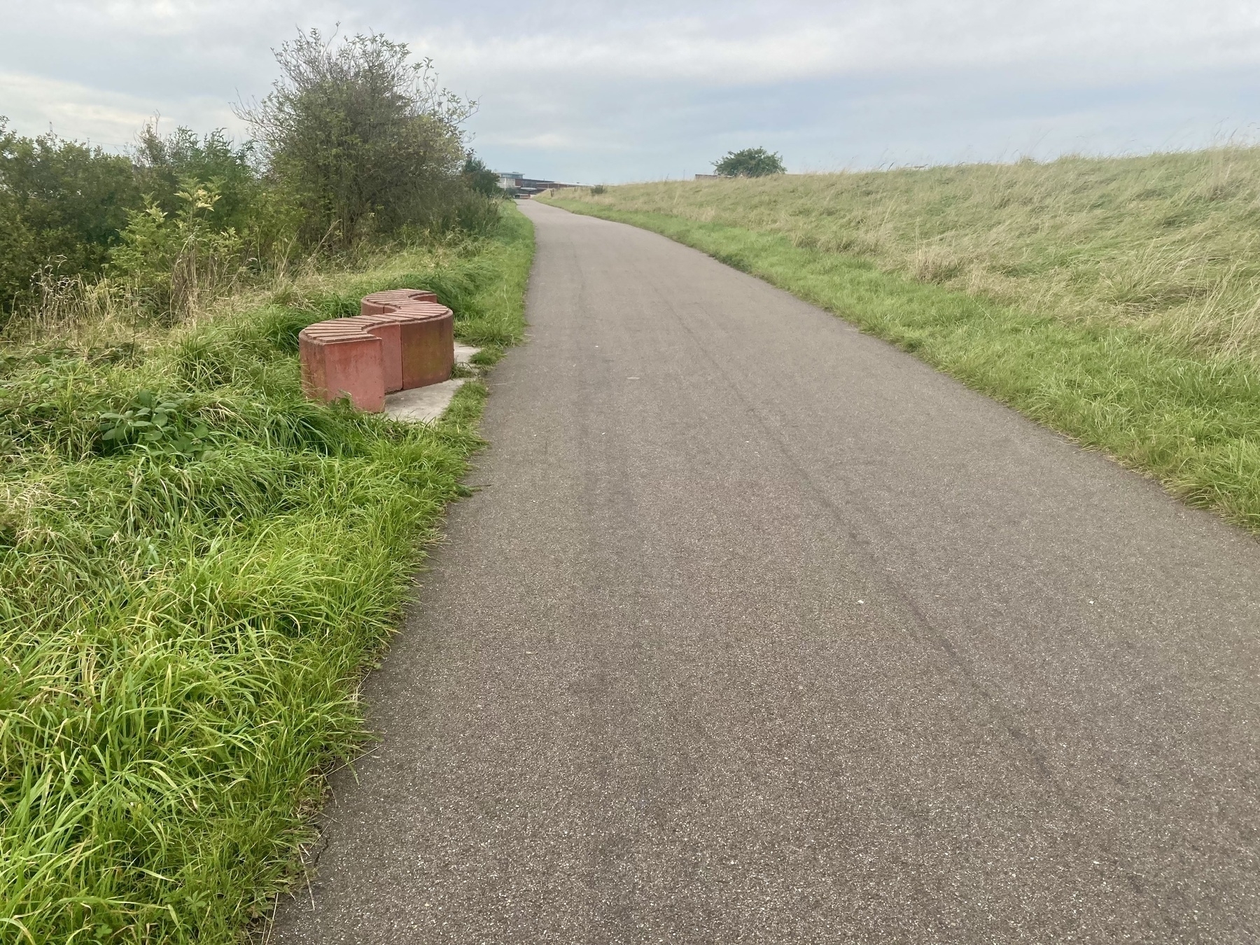 Een verhard pad slingert door grasvelden met een rode golvende bank langs de zijkant.