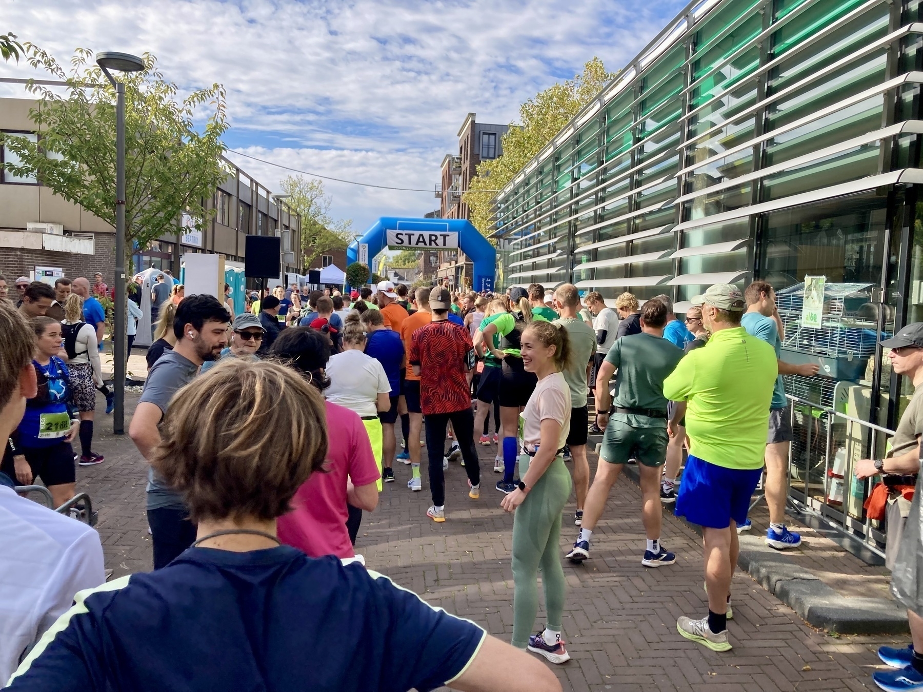 Een groep mensen is verzameld bij een startlijn voor een race in een stedelijke buitenomgeving.