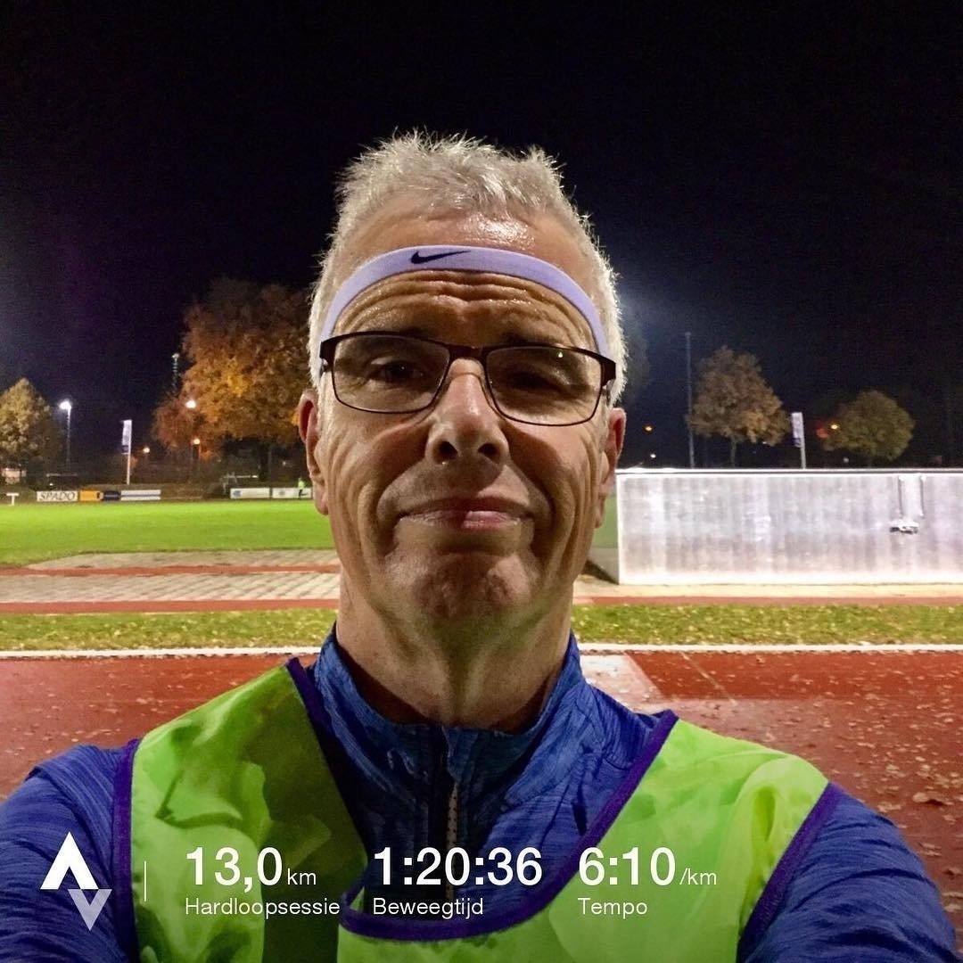 Een man in atletische uitrusting maakt een selfie op een baan, met tekst onderaan met zijn hardloopstatistieken: 13,0 km afstand, 1:20:36 duur en 6:10 min/km tempo.