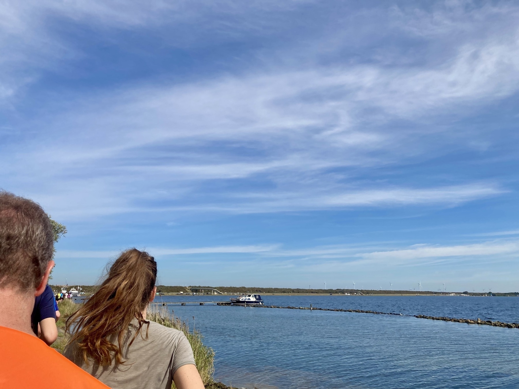 Een groep mensen geniet van een schilderachtig uitzicht op een rustig waterlichaam met een verre boot en een uitgestrekte lucht.