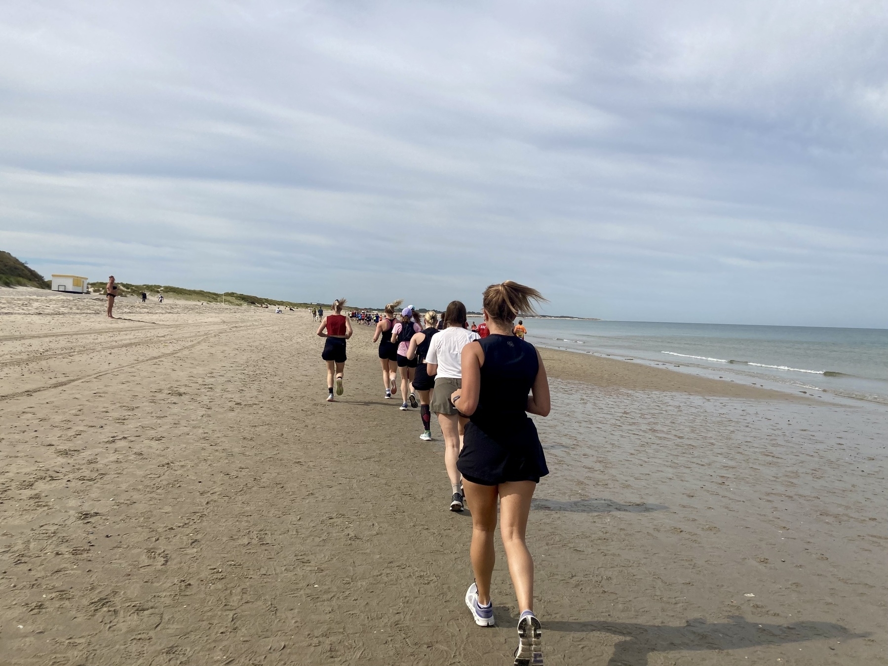 Een groep mensen rent langs een zandstrand in de buurt van de kustlijn.