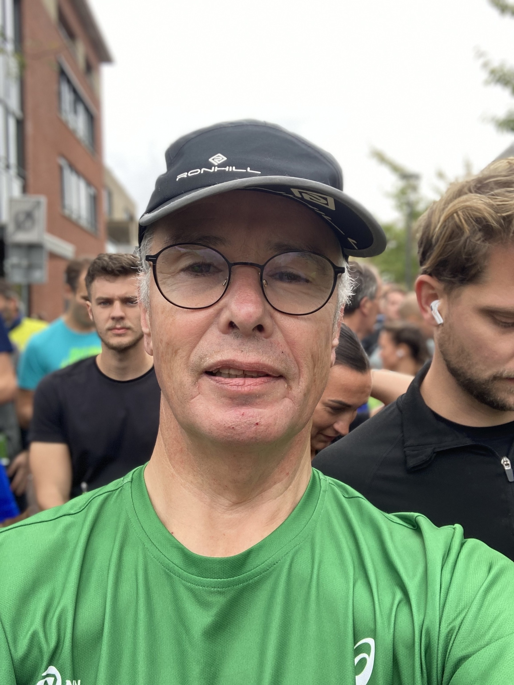 Een man met een groen shirt en een zwarte pet staat buiten in een menigte mensen.