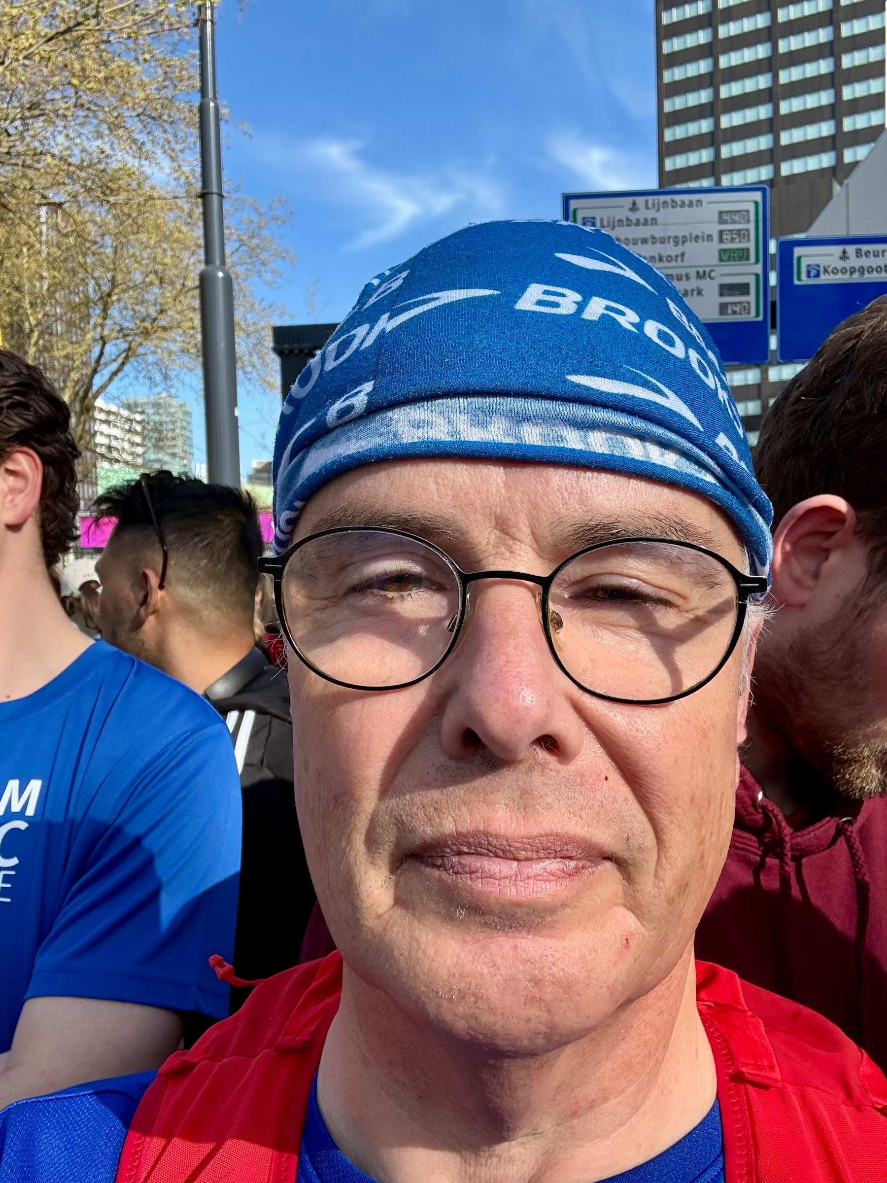 Een persoon met een bril en een blauwe hoofdband staat buiten tussen een groep mensen.