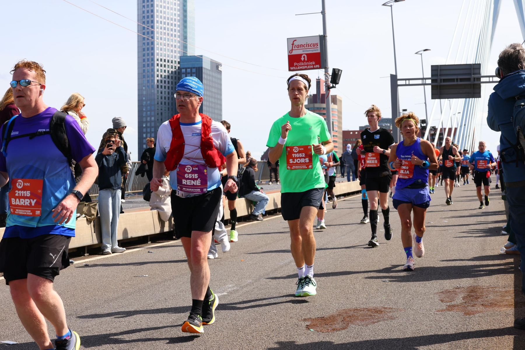 Hardlopers nemen deel aan een race op een stadsbrug, waarbij sommigen borstnummers en atletische uitrusting dragen.