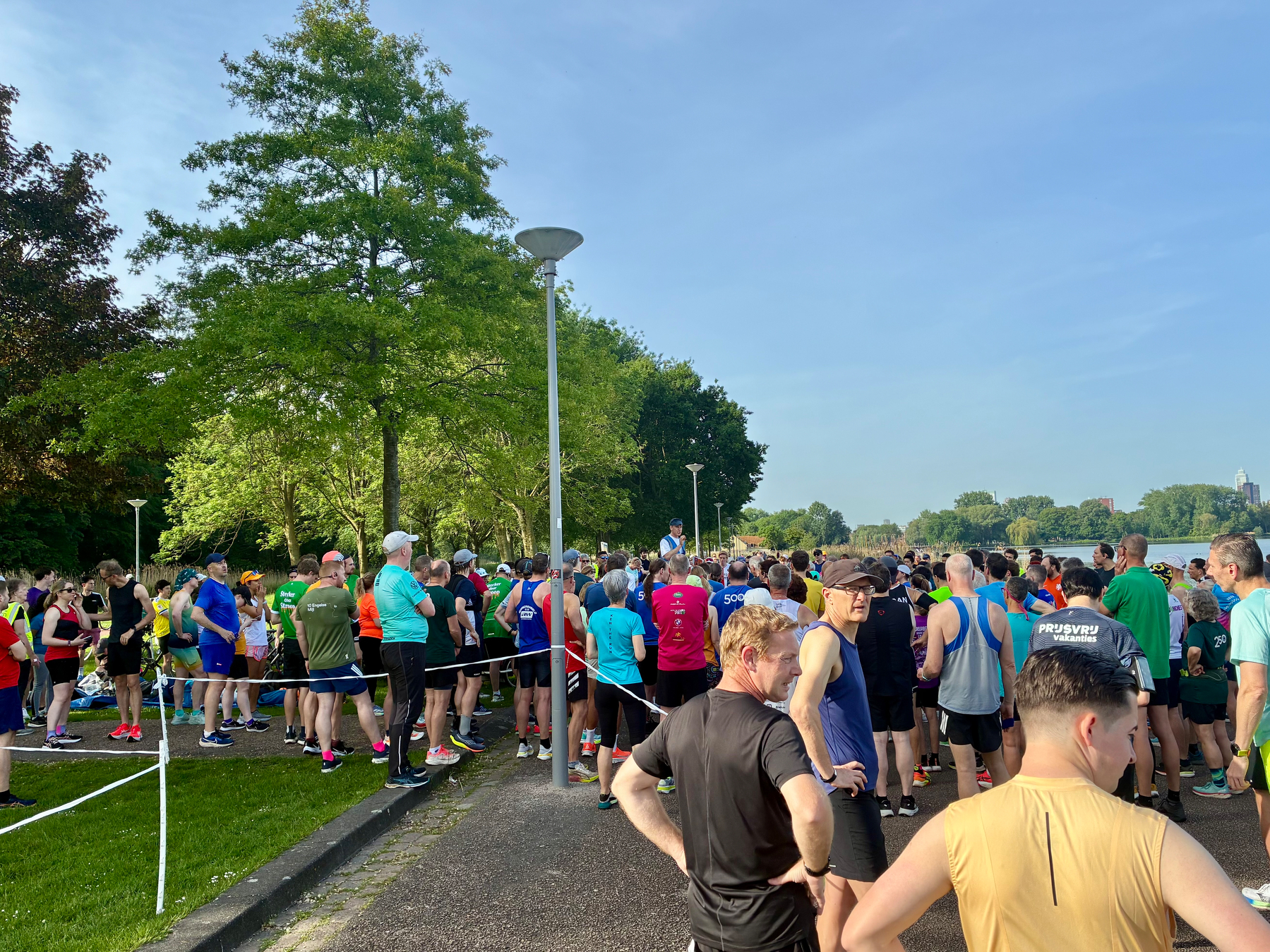 Een grote groep mensen verzamelt zich buiten en bereidt zich voor op een hardloopevenement op een zonnige dag.