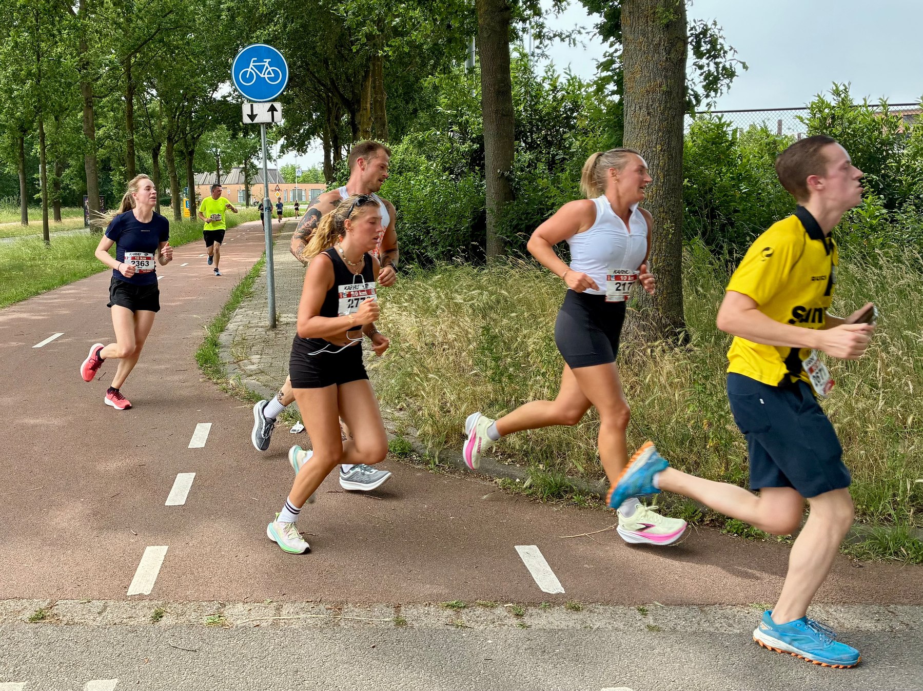 Een groep mensen rent op een fietspad tijdens een race in een buitenomgeving.