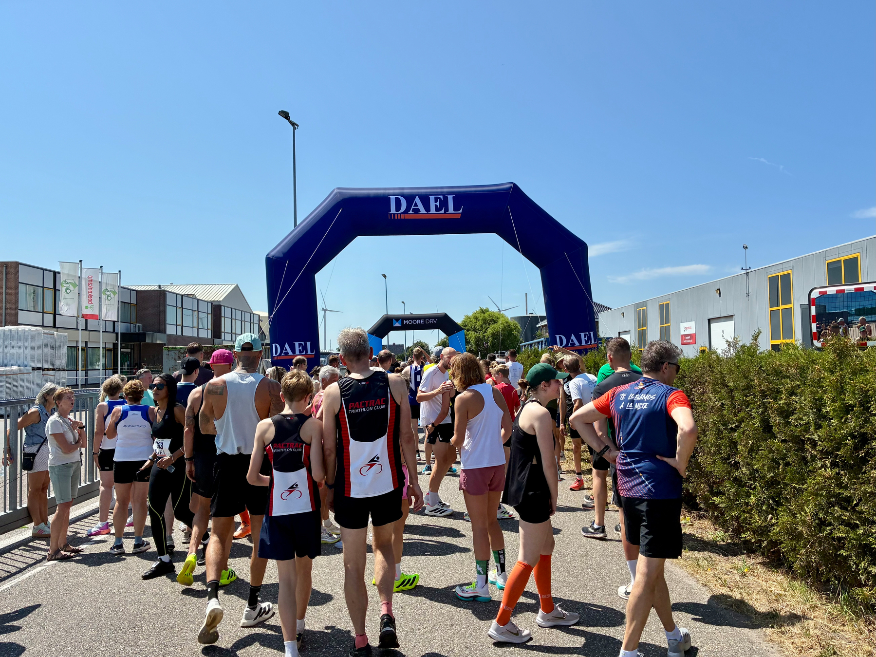 Een groep mensen verzamelt zich op een zonnige dag in de buurt van opblaasbare bogen met het label DAEL, waarschijnlijk aan het voorbereiden van of deelnemen aan een race of sportevenement.
