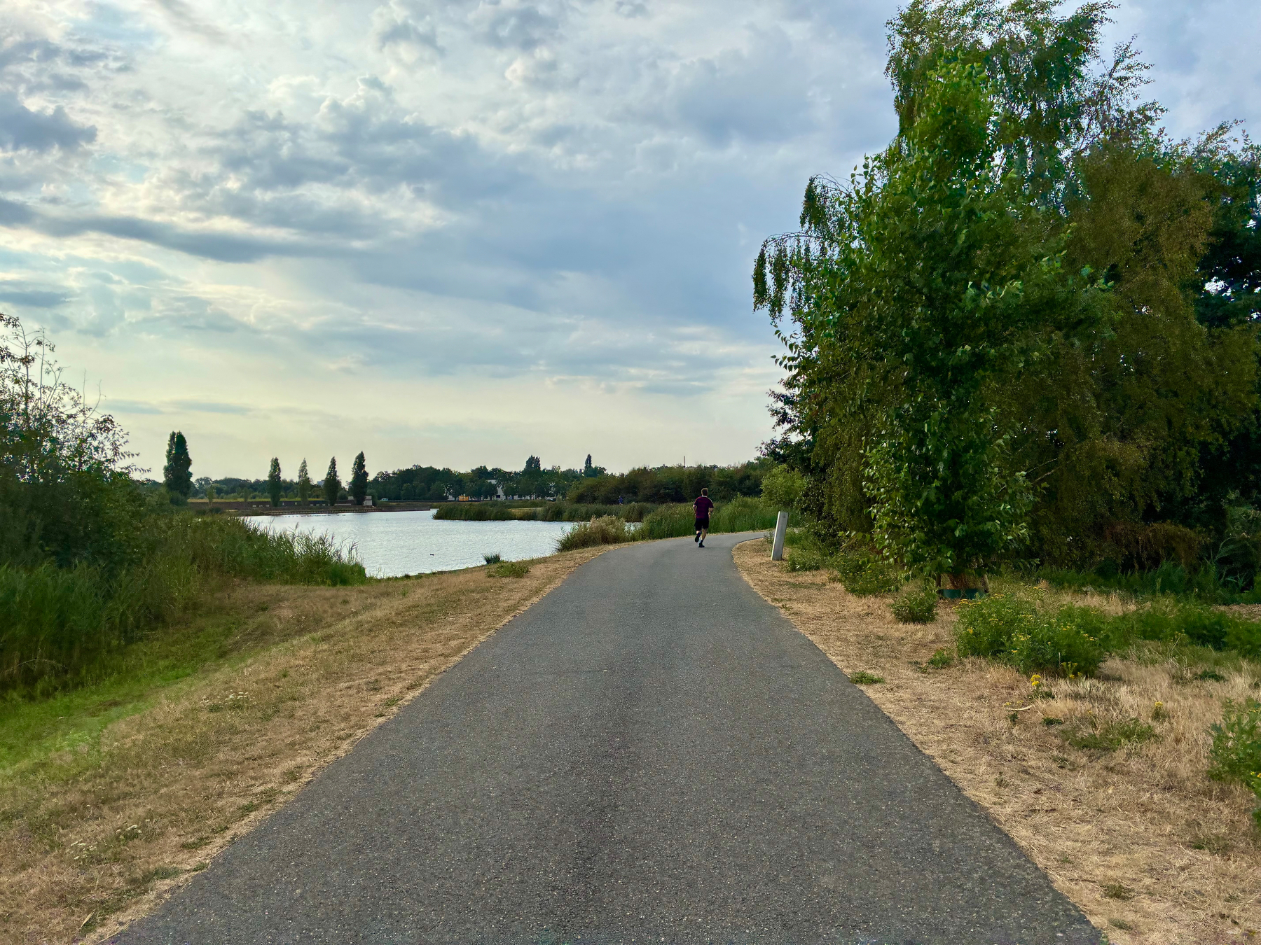 Een persoon loopt hard over een verhard pad naast een waterlichaam onder een gedeeltelijk bewolkte lucht.