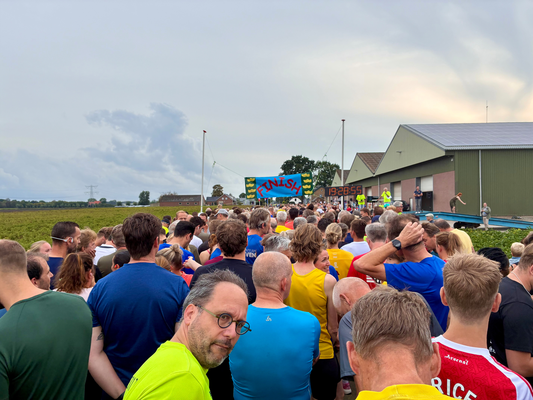 Een menigte mensen verzamelt zich in de buurt van een finishbanner in een buitenomgeving, met enkele personen die atletische kleding dragen.
