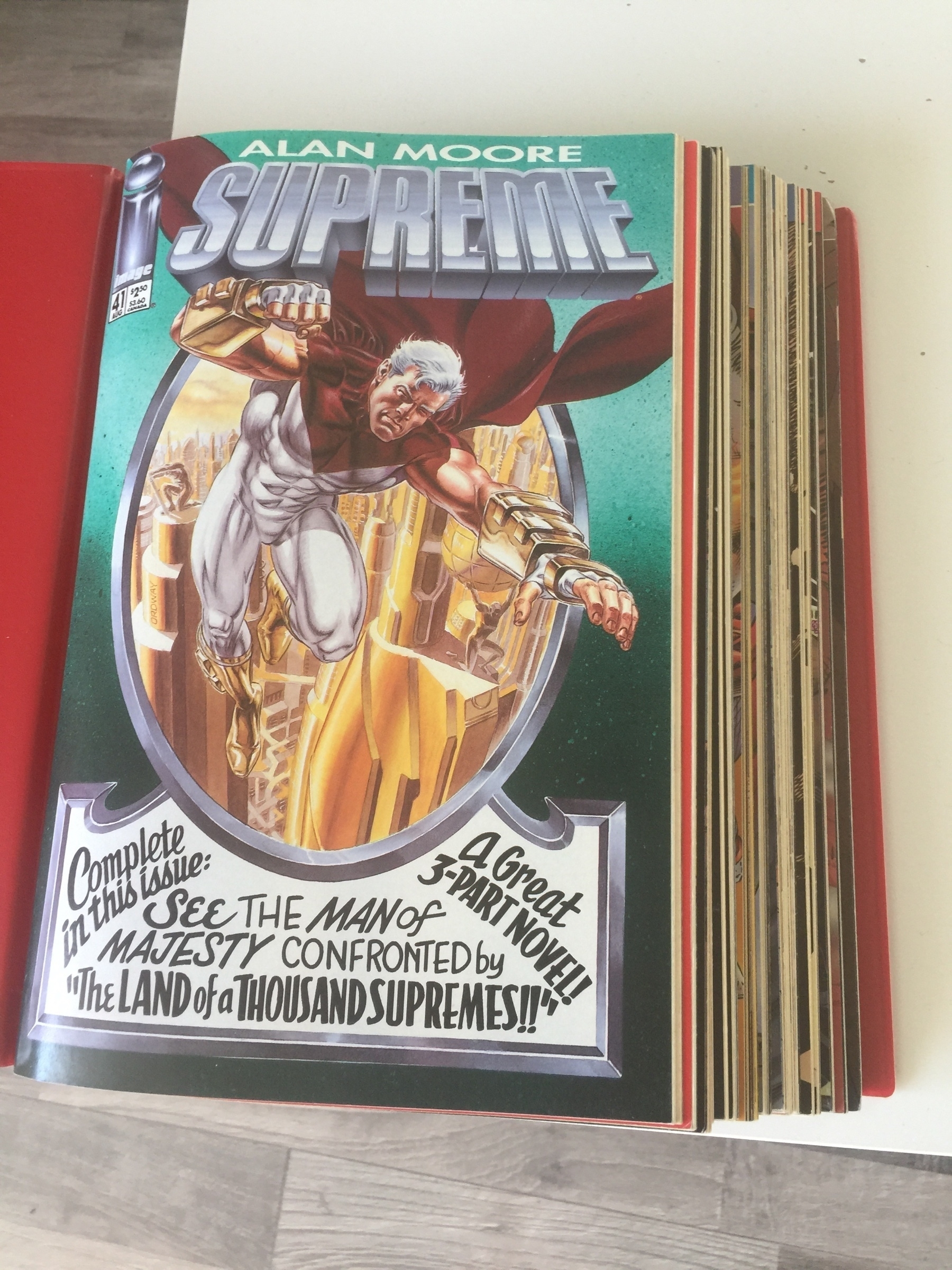 A binder containing a stack of comics. The topmost one is titled "Alan Moore: Supreme"