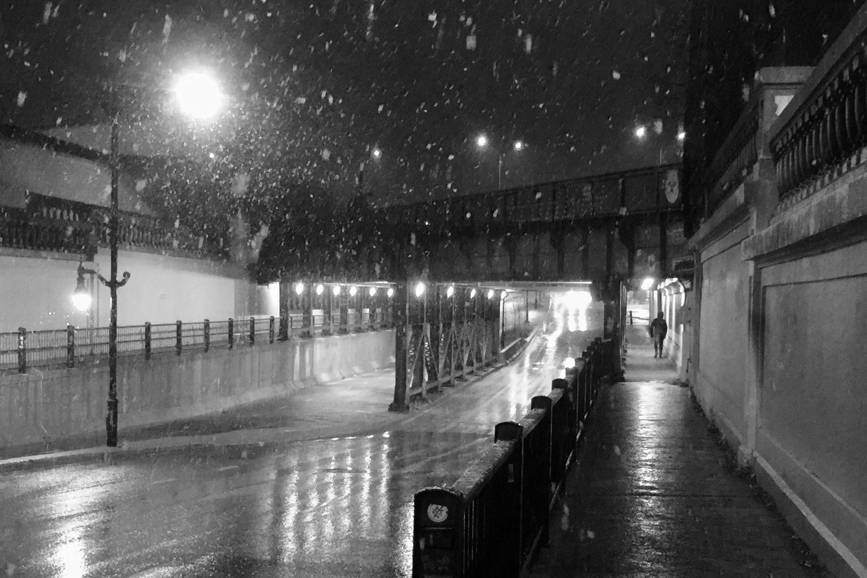 It’s snowing and somebody is walking through an underpass under a railway bridge.