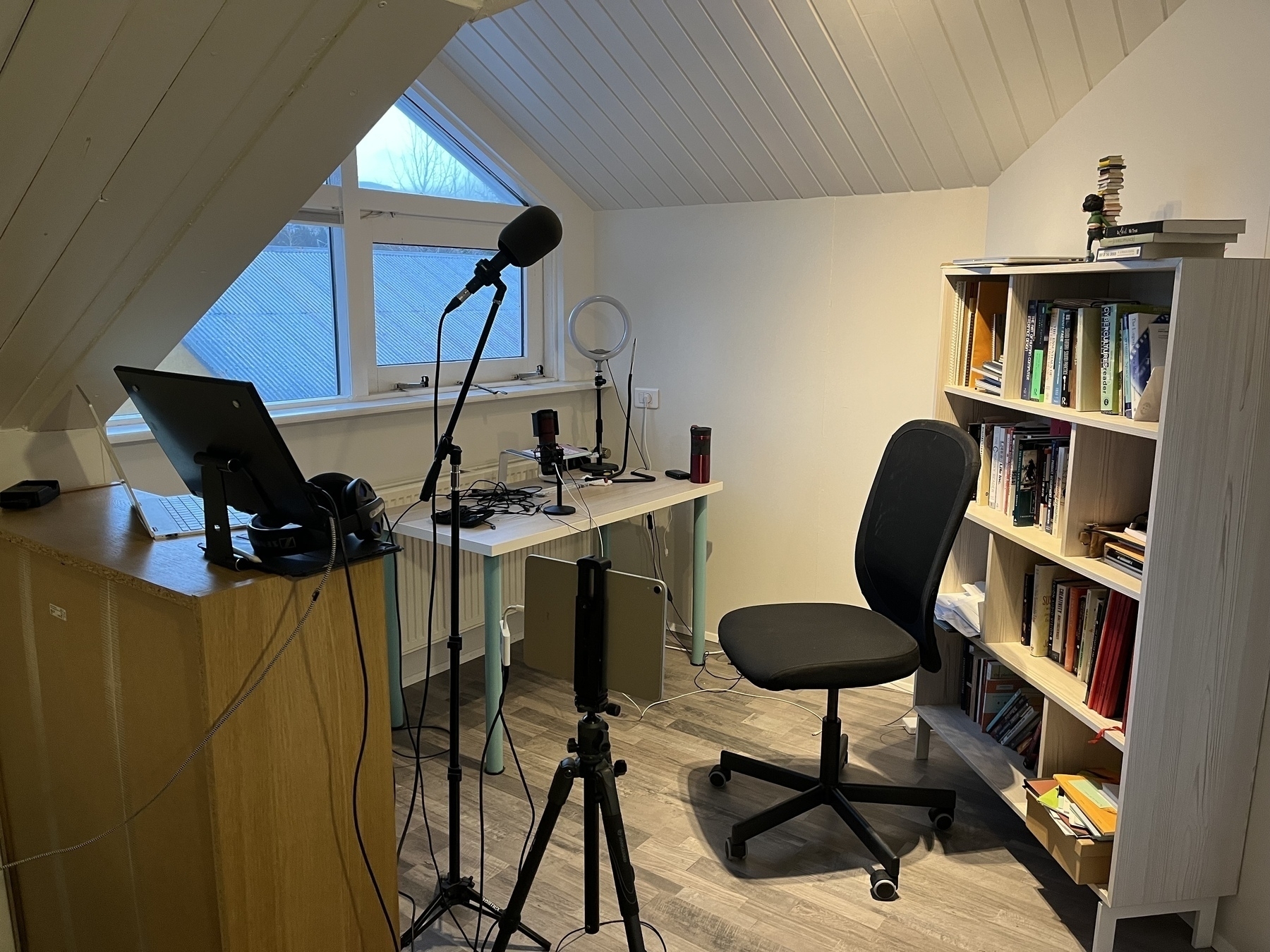 A home office with a nice microphone on a stand a chair and some shelves. 