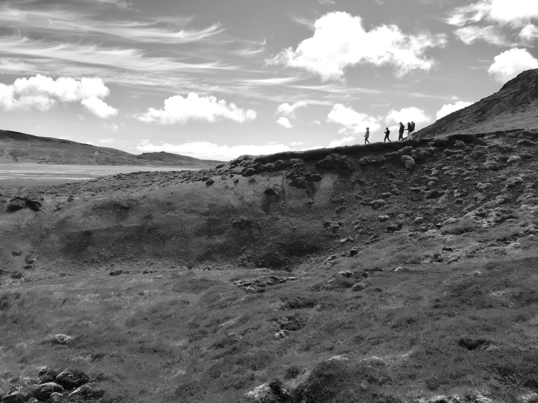 A group of tourists walk along a ridge, appearing in silhouette