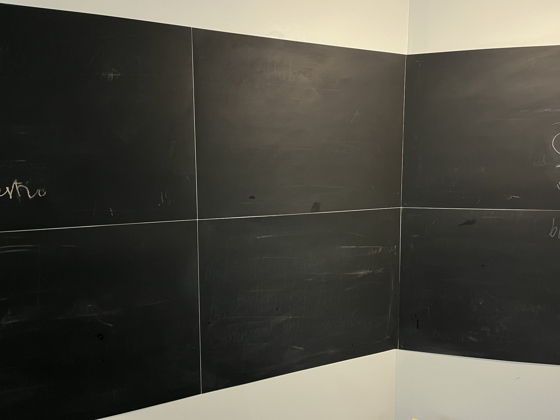 A photo of several blackboard tiles on a corner wall. 