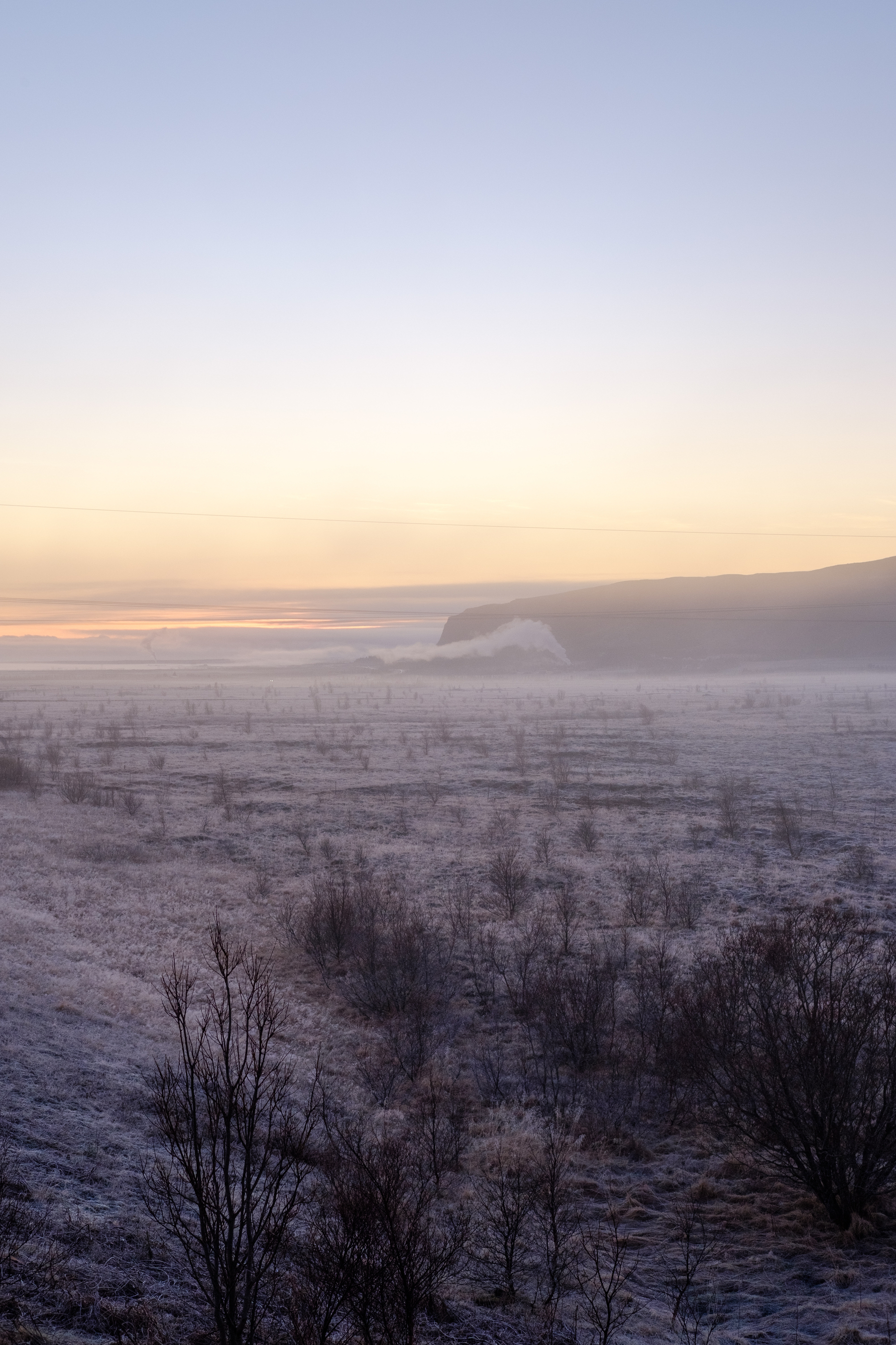 A view of steam rising from a geothermal area in the distance. Frost covers the ground