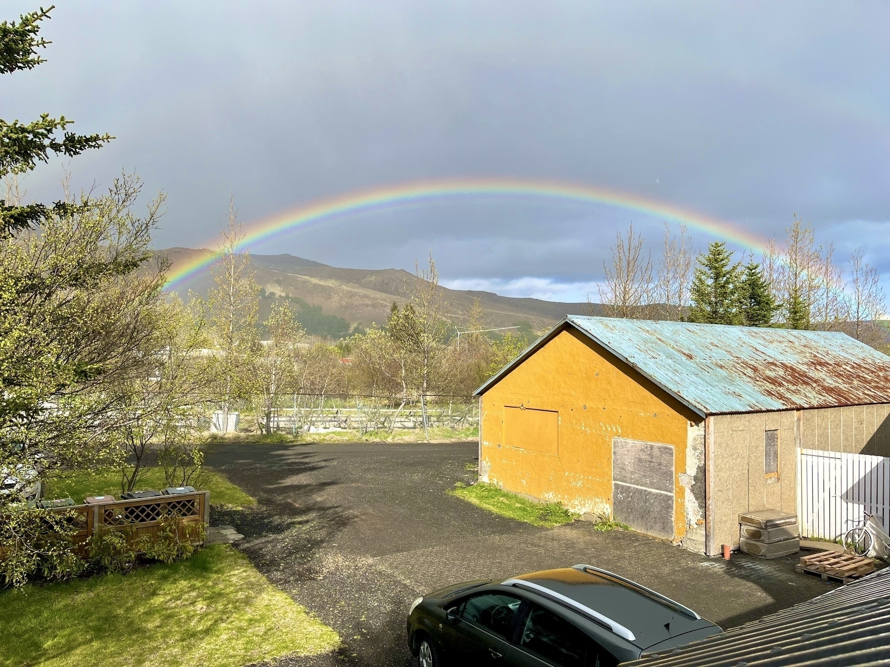 A rainbow over a commercial garden in the background. In the foreground there is a small old dilapidated warehouse that has seen better days.