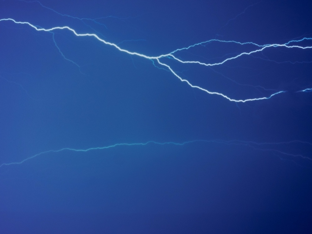 A striking bolt of lightning illuminates the sky against a deep blue background.