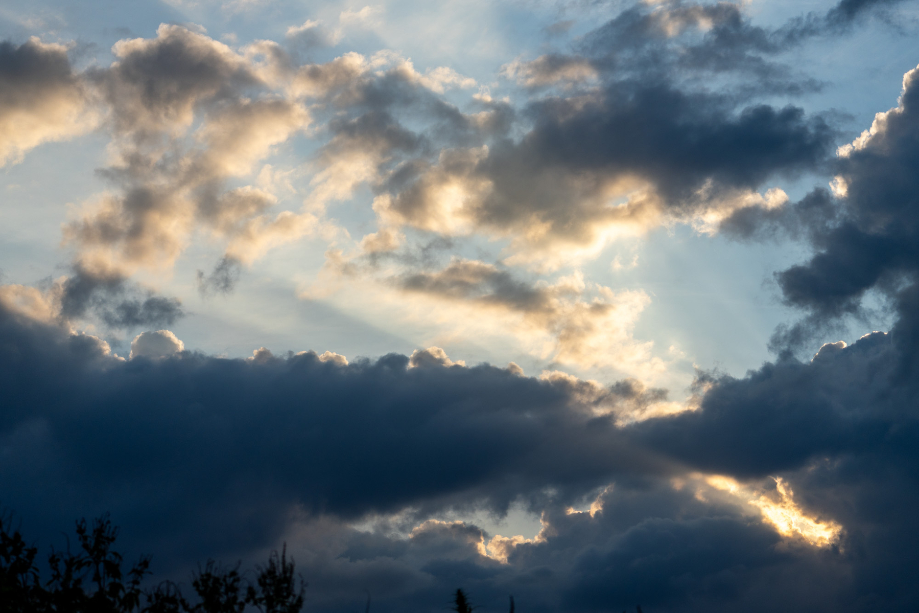Dark clouds fill the sky with sunlight peeking through, casting dramatic shadows and light beams.