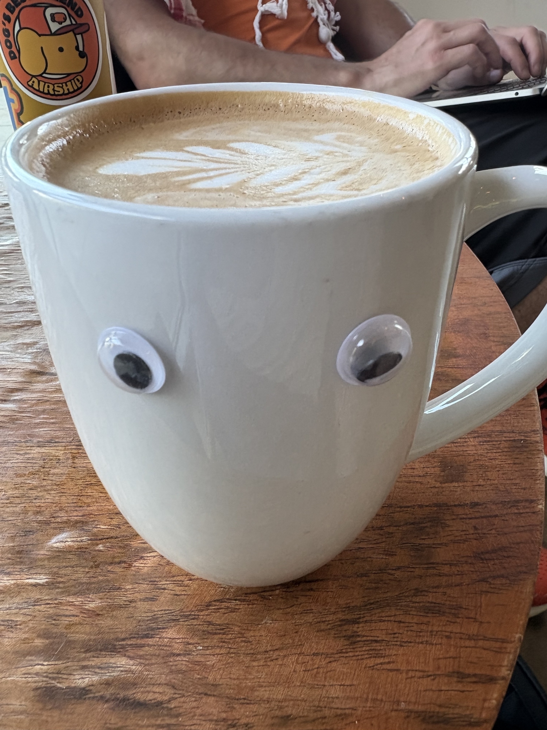 A mocha in a cup with latte art and googly eyes on the side. 