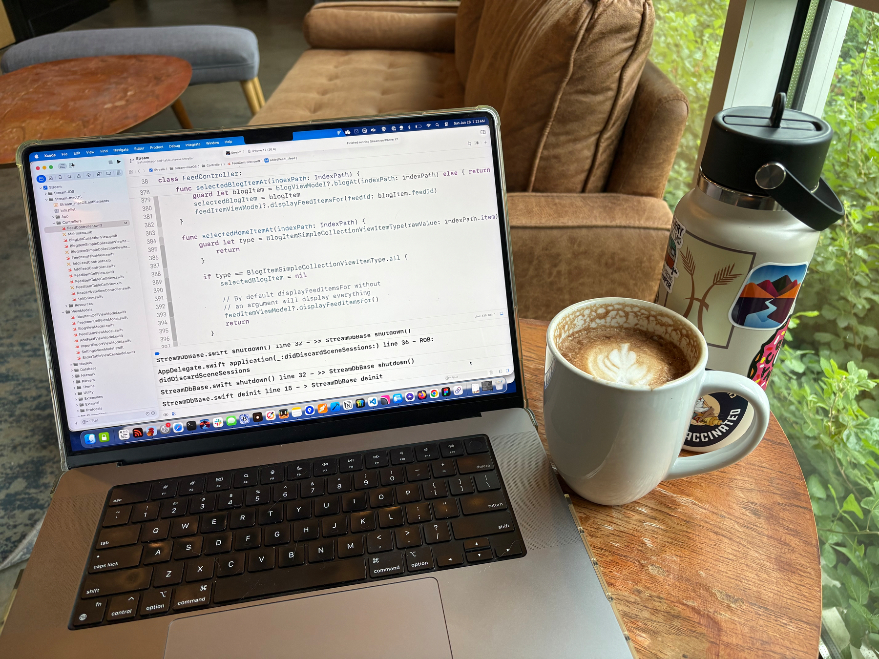 MacBook Pro next to a mug of coffee and a water bottle decorated in stickers.