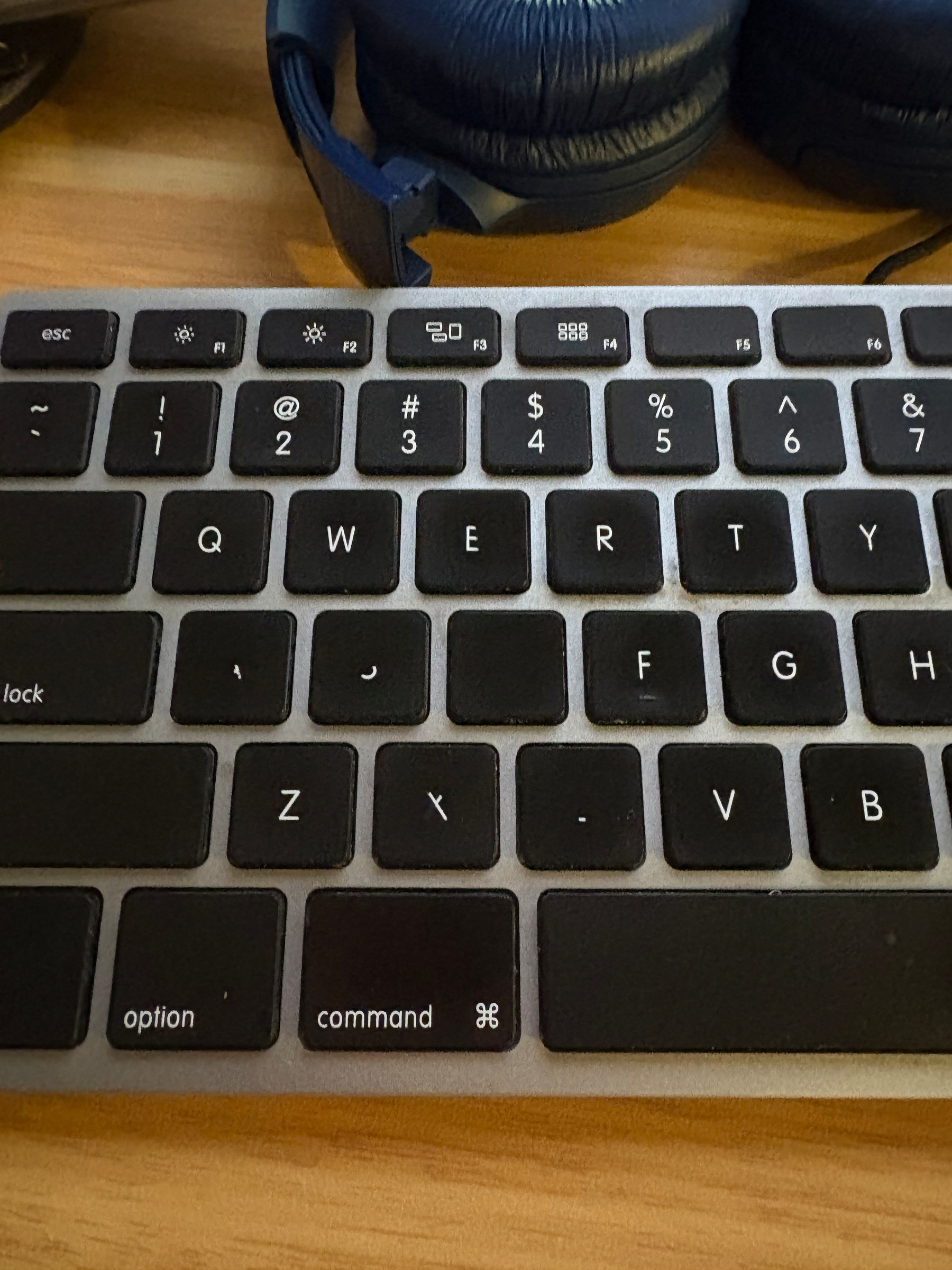 A silver bodied keyboard with black keys. Some of the keys are missing letters, others are partially missing.