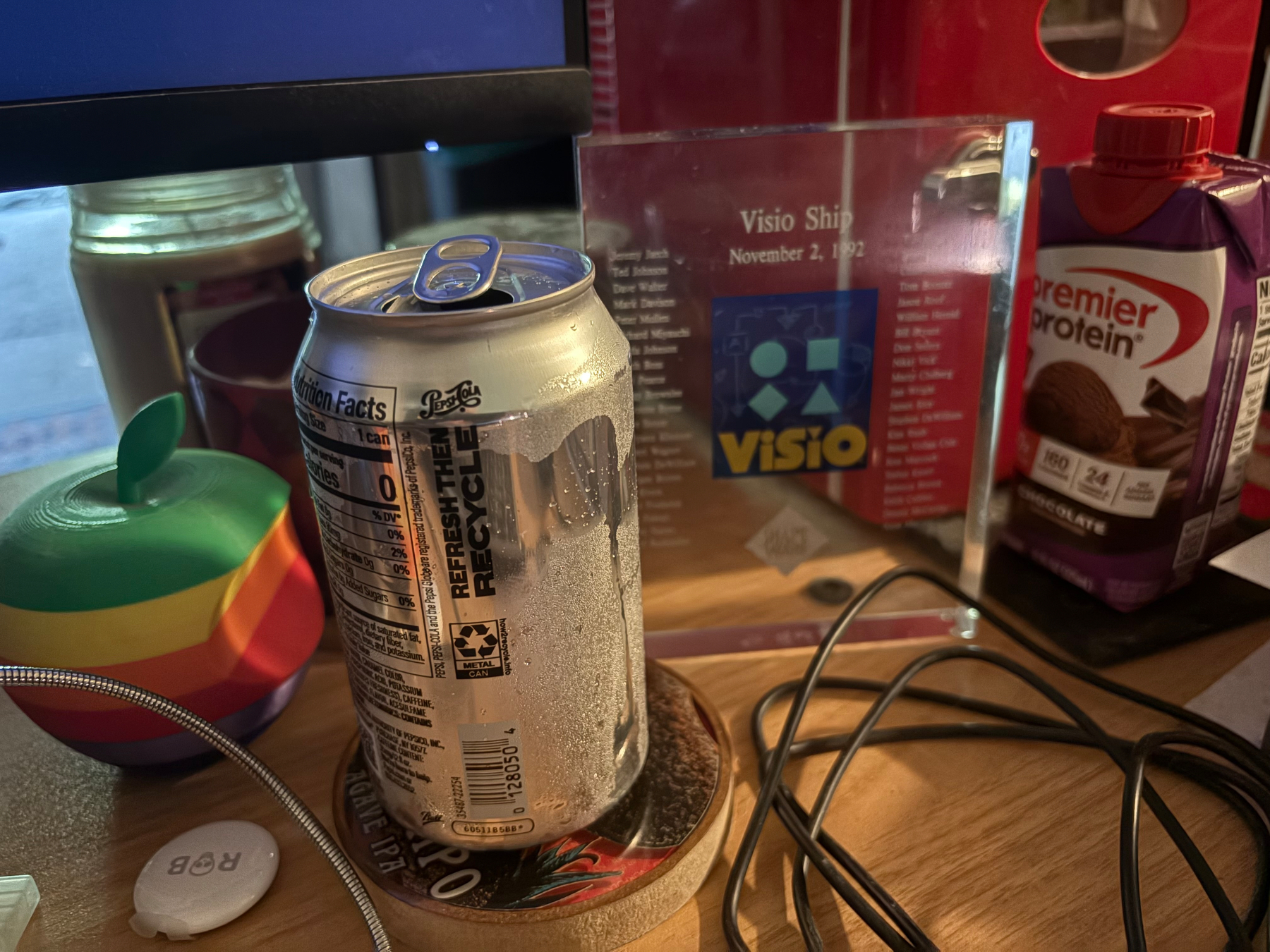 In the shot we have a 3D printed Apple in six colors, an AirTag printed with R💀B, a Diet Pepsi, my Visio 1.0 tombstone, a mouse cable, a little red fridge, an empty protein shake box, and some candles in the background. 🤣