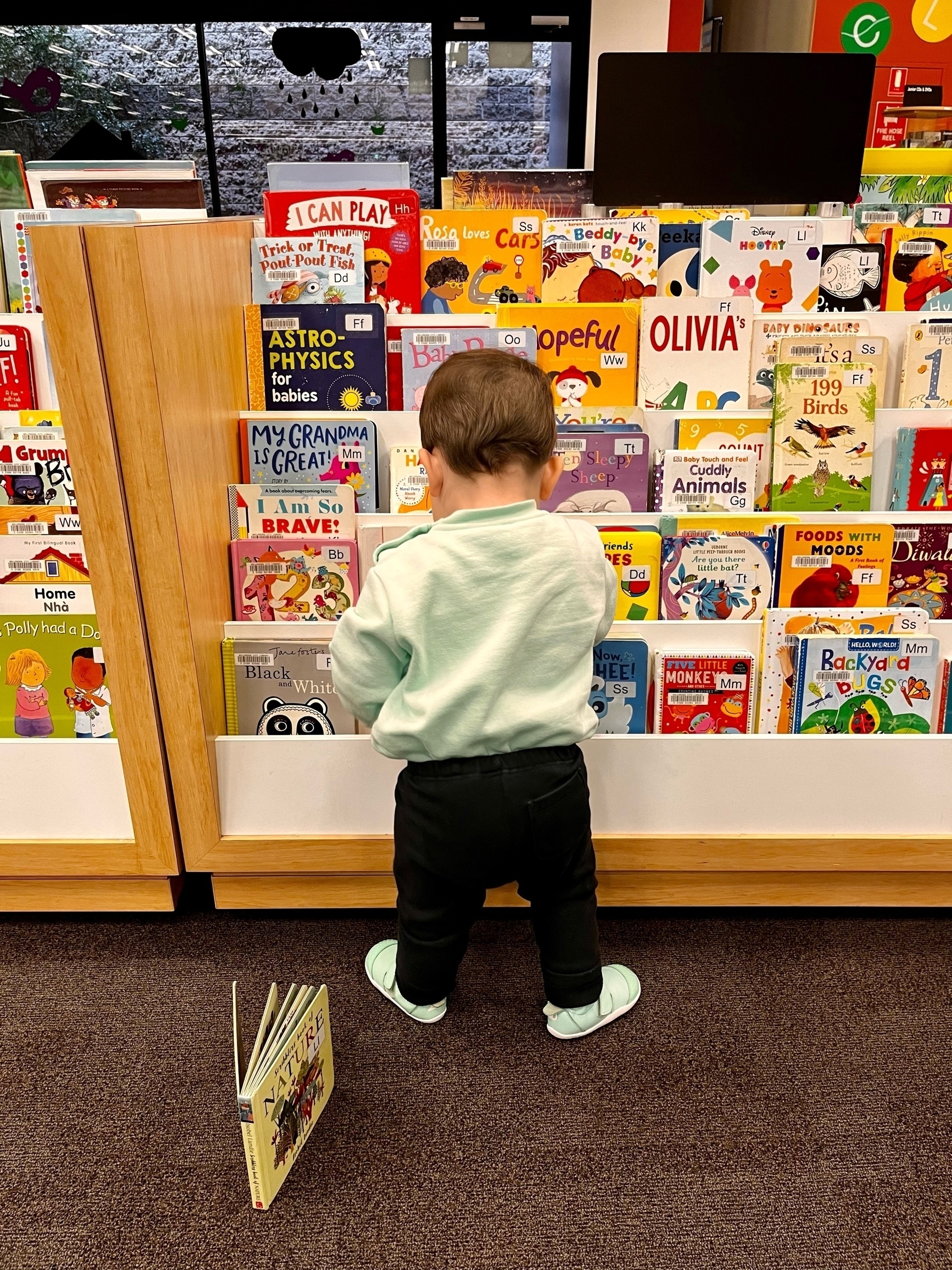 A baby exploring a kids' bookshelf at a library