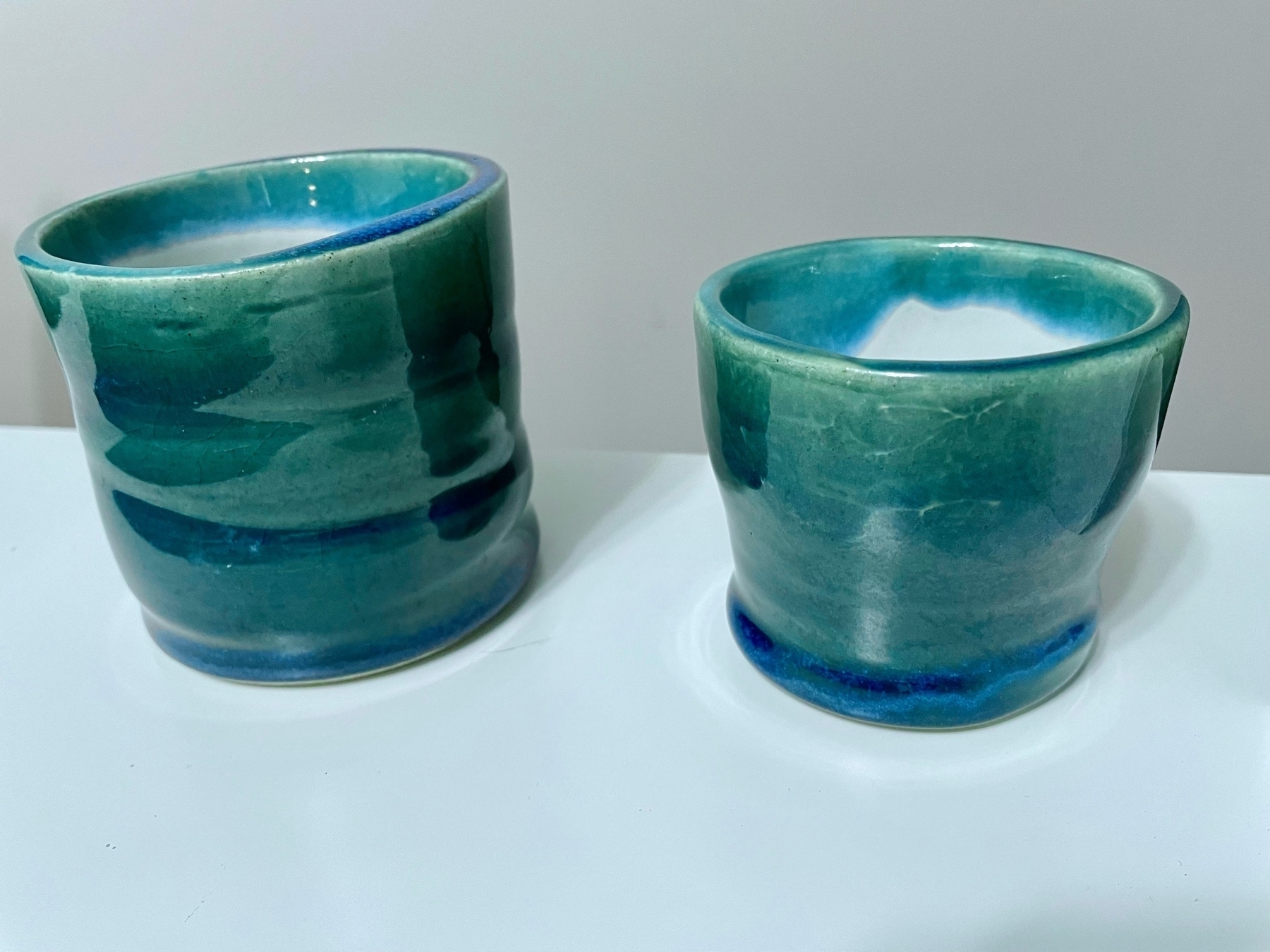 two hand made pottery cups with a blueish green glaze