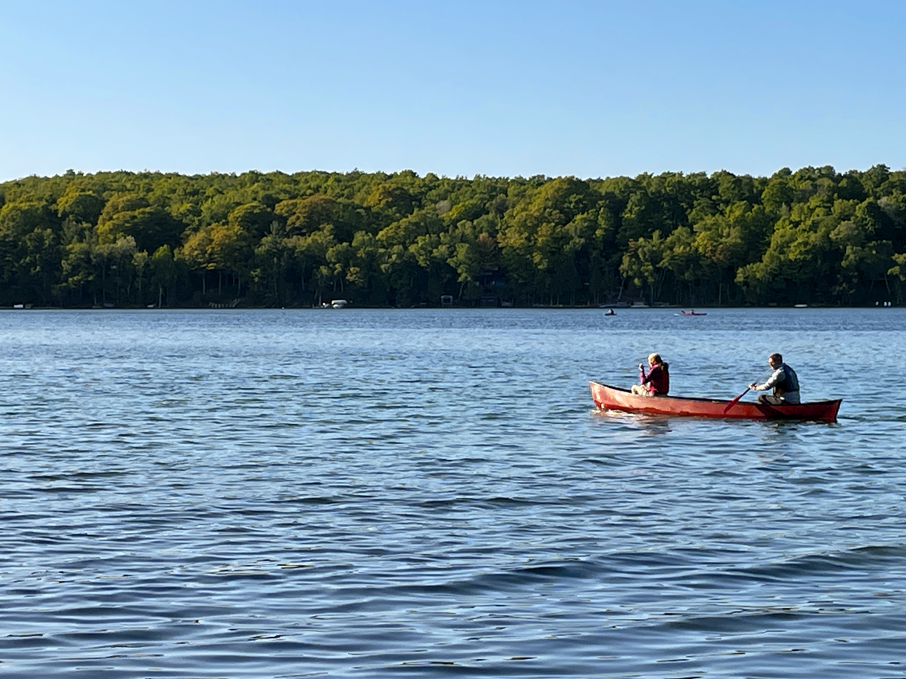 Two people paddling a canoe on a lake with trees on the far shore