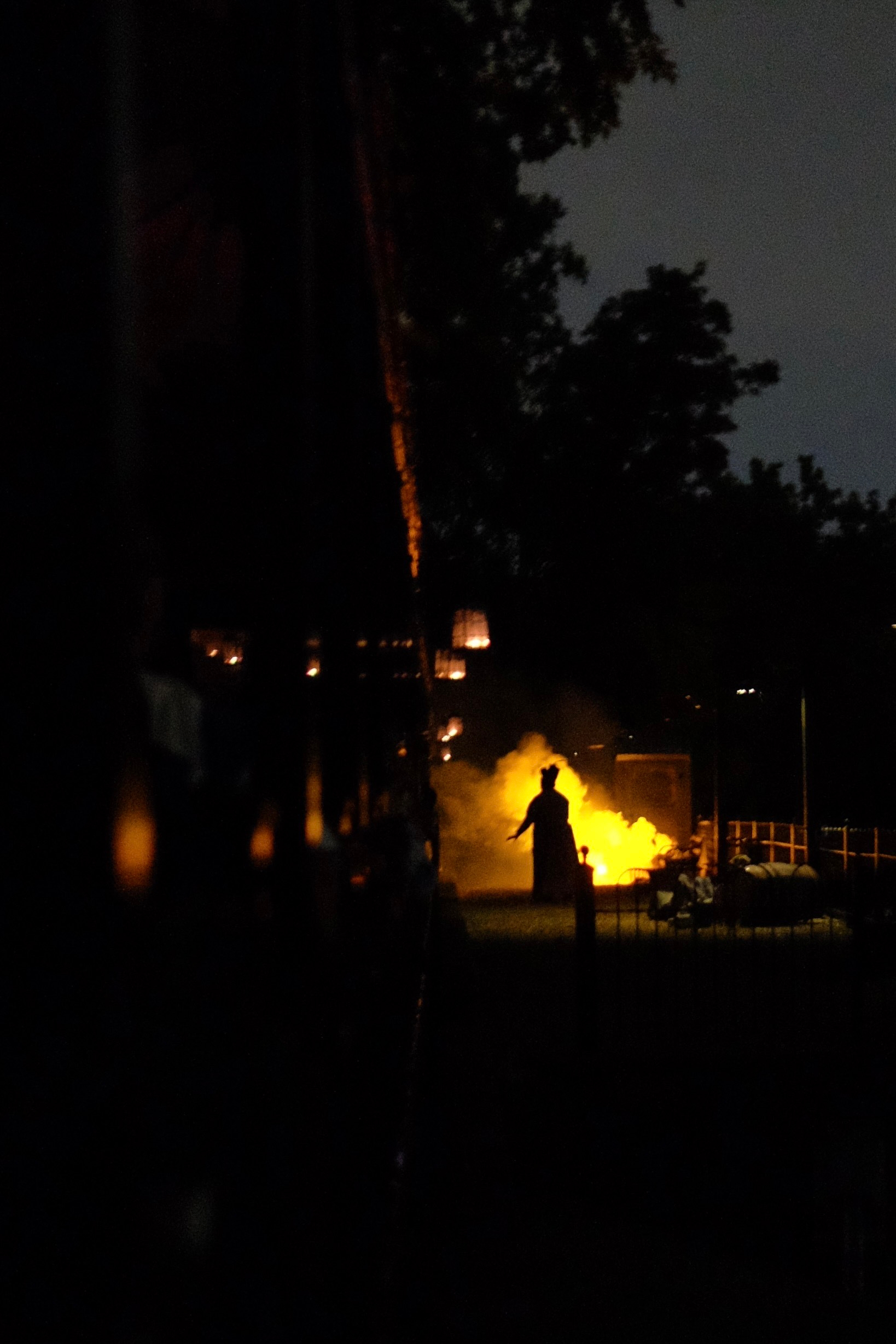 A silhouette of a woman stands in bright yellow-orange smoke at a dark, outdoor train stop.