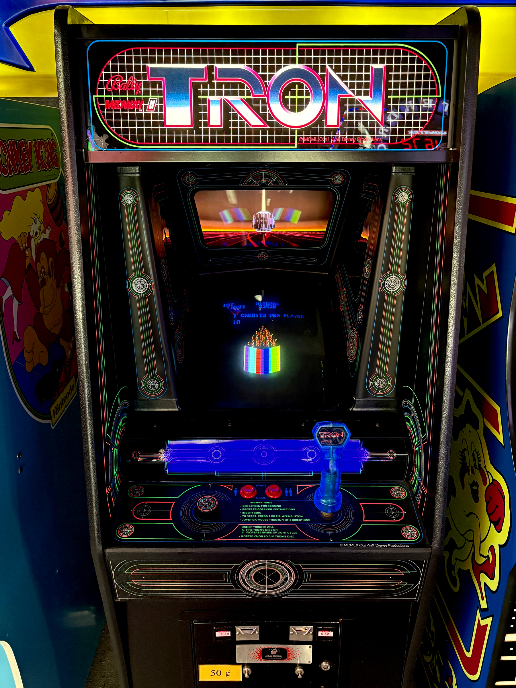 An arcade machine for the classic video game Tron features neon lights and a joystick, surrounded by a retro gaming atmosphere.