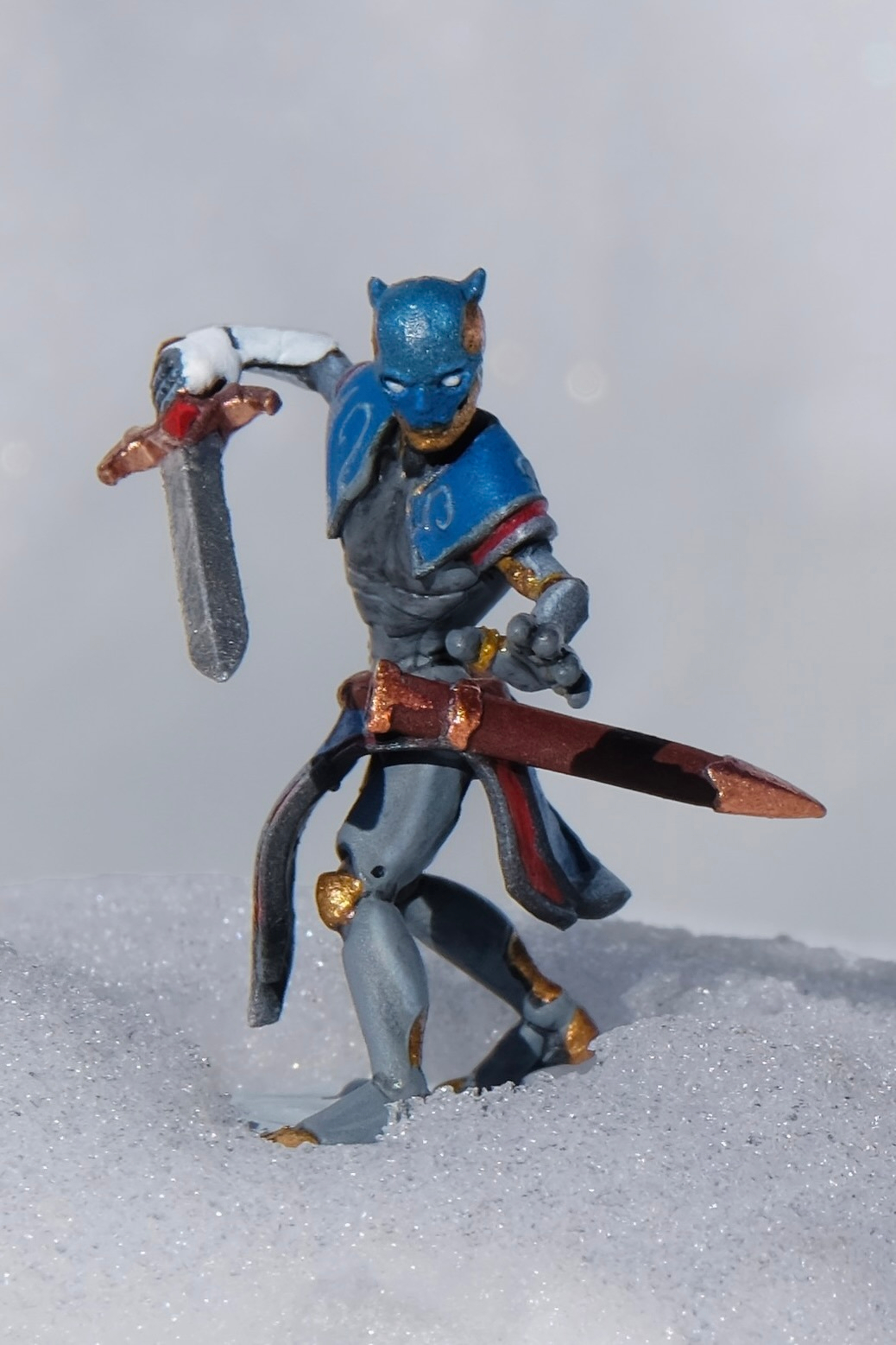 A dungeons and dragons miniature of a warforged in blue armor is posed holding a sword, standing on snow.