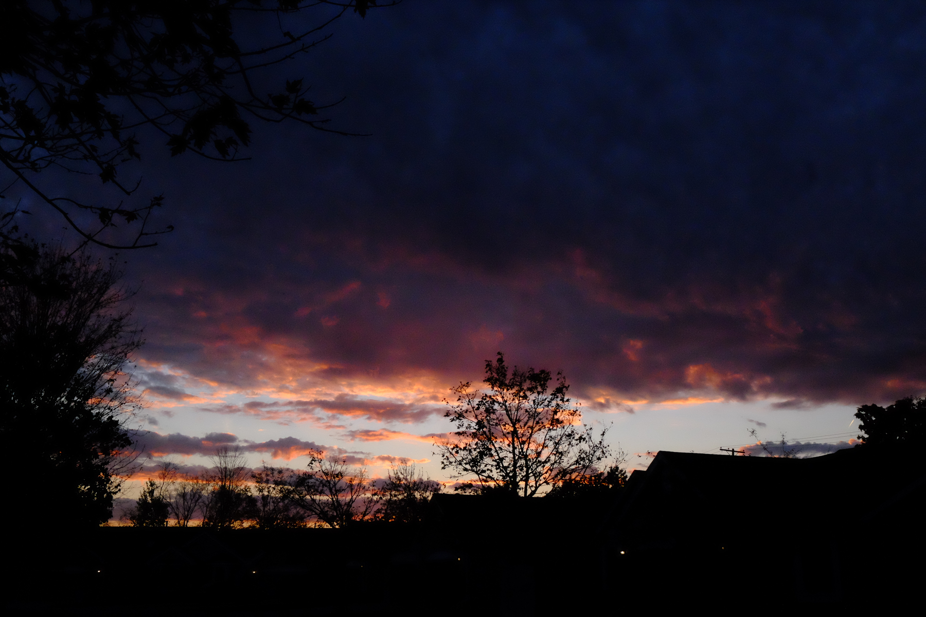 A dramatic sunset sky with dark clouds and silhouettes of trees and rooftops is visible.