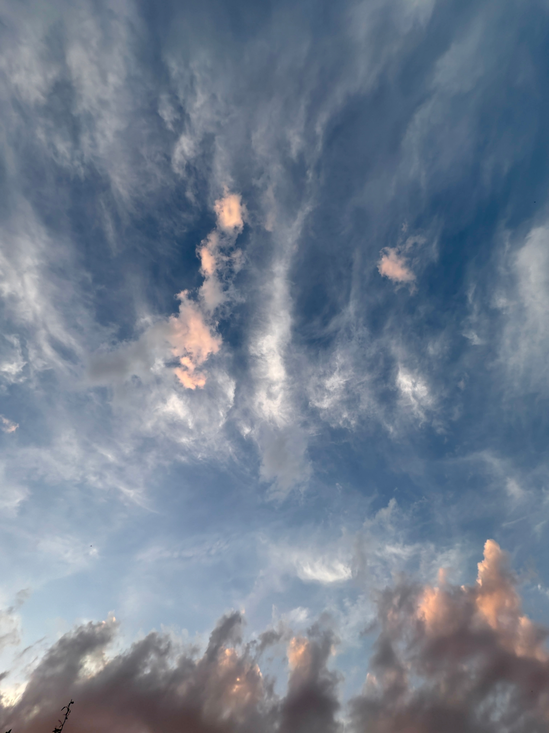 A sky filled with wispy clouds illuminated by soft hues of pink and orange during sunset or sunrise.