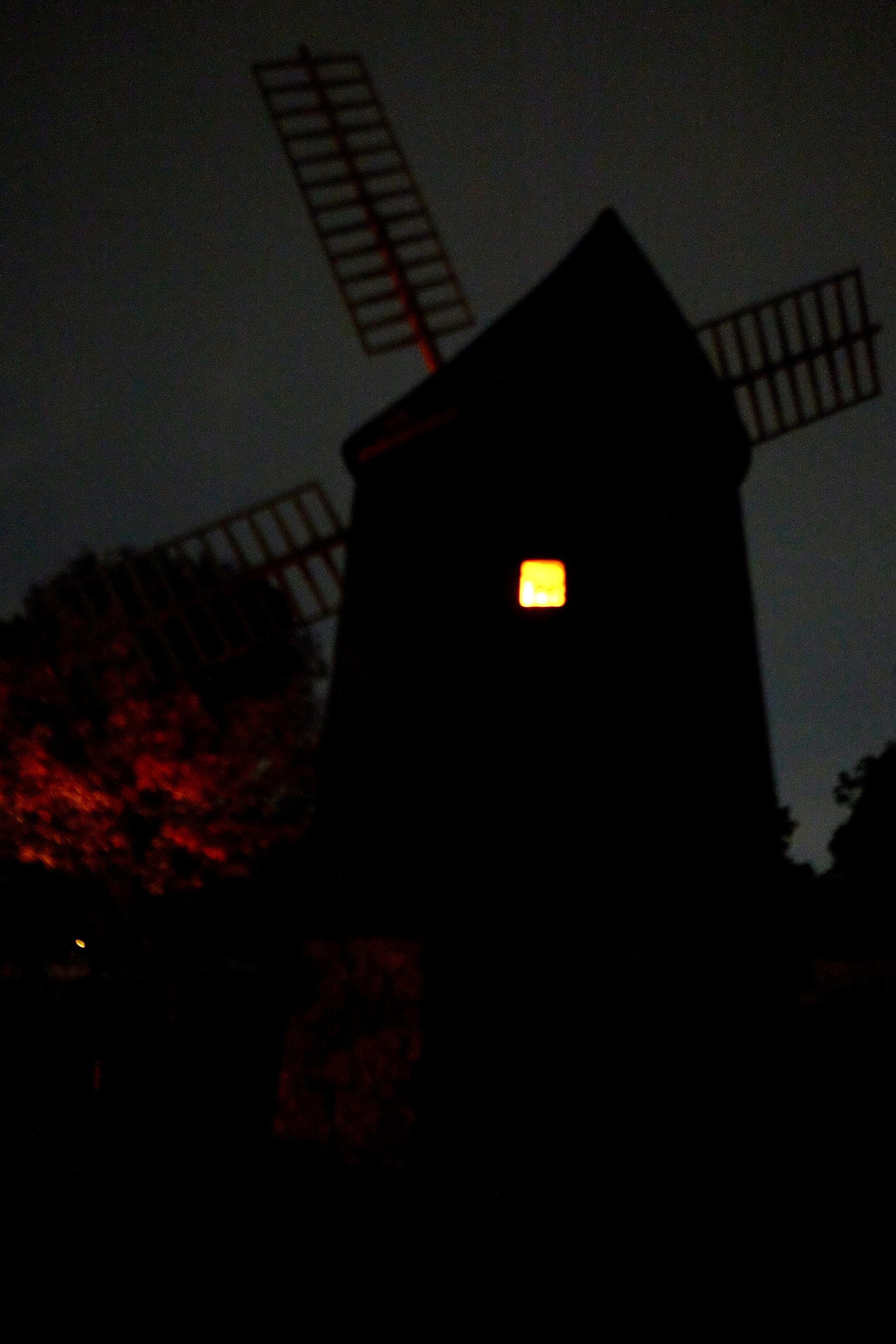 A windmill stands silhouetted against the night sky with a single illuminated window.