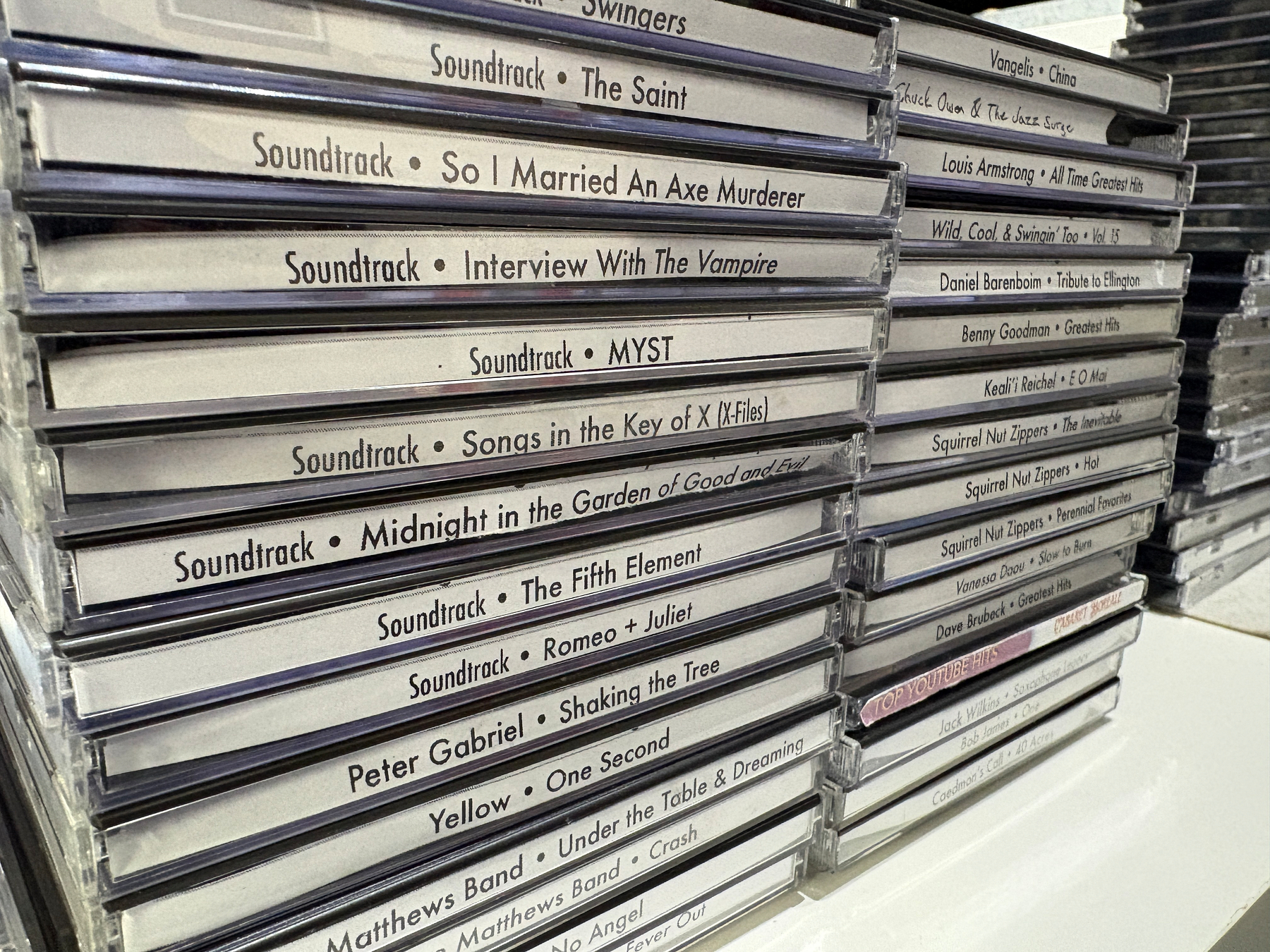 A collection of stacked CD cases featuring soundtracks and albums from various artists and movies is displayed on a shelf.