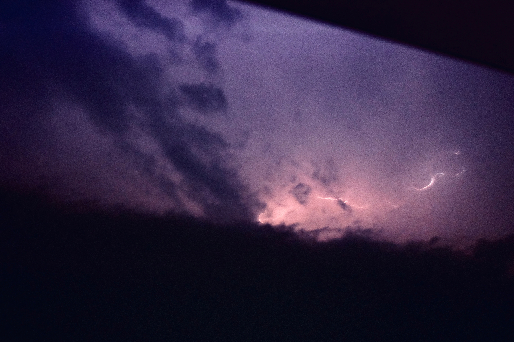 A dark sky is illuminated by a lightning strike partially obscured by clouds.