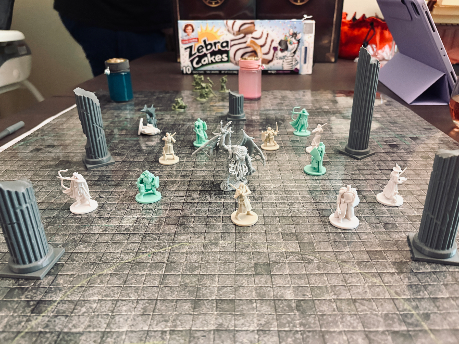 A tabletop game setup features various miniature figures arranged on a grid.