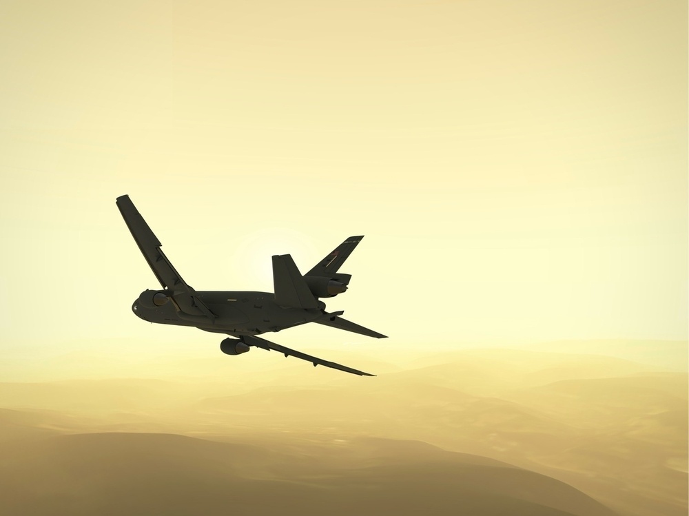 A silhouette of an airplane is flying against a hazy, golden sky with distant hills visible.