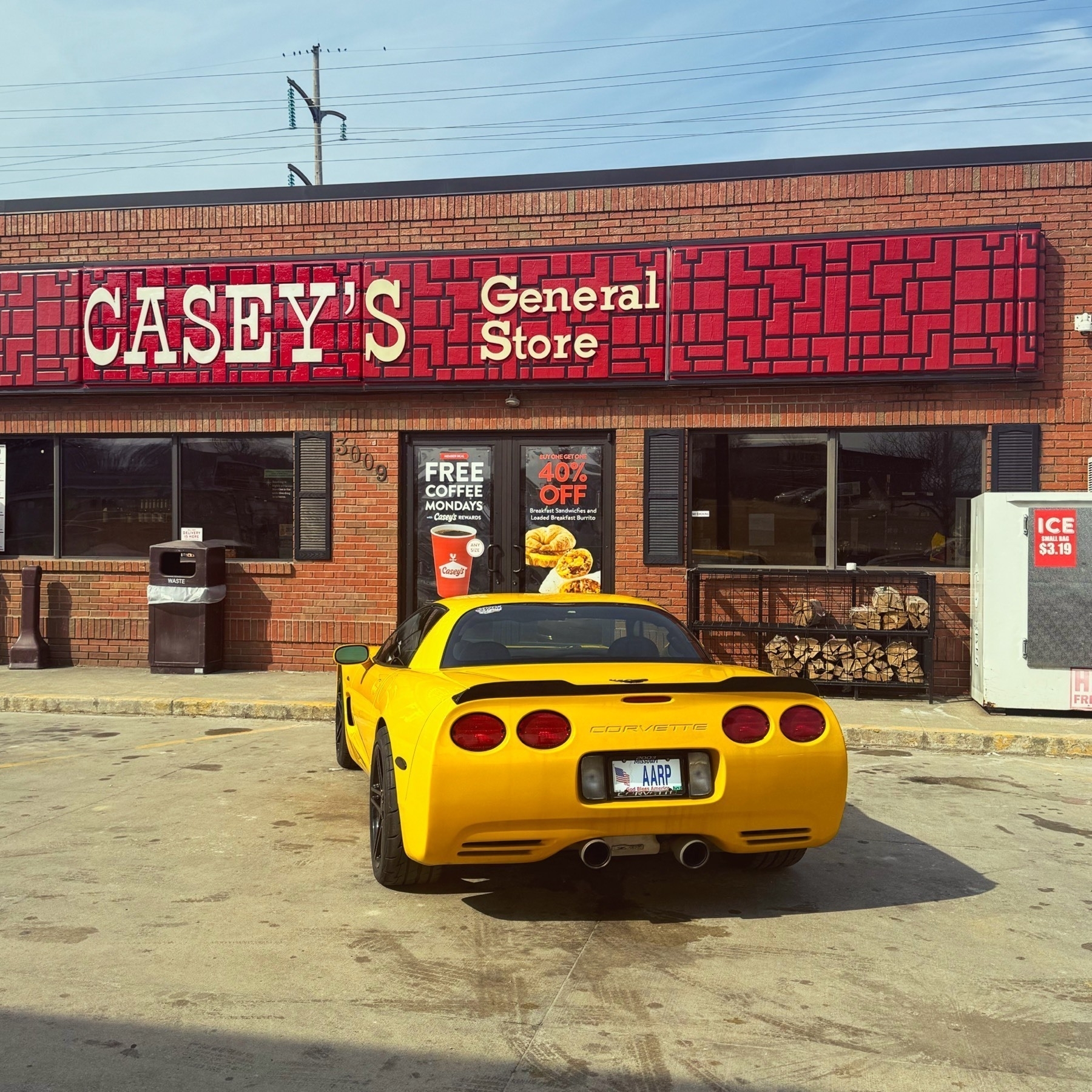 Bright yellow C-5 Corvette parked in front of a Casey's General store wearing the license plate "AARP."