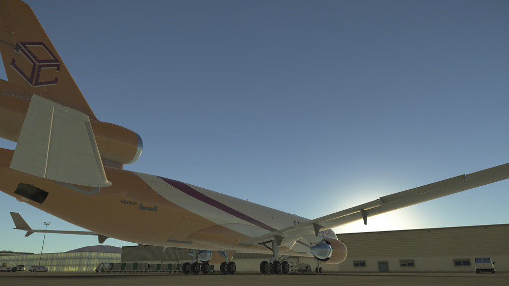 A large airplane is parked near a hangar under a clear blue sky, viewed from a low angle.