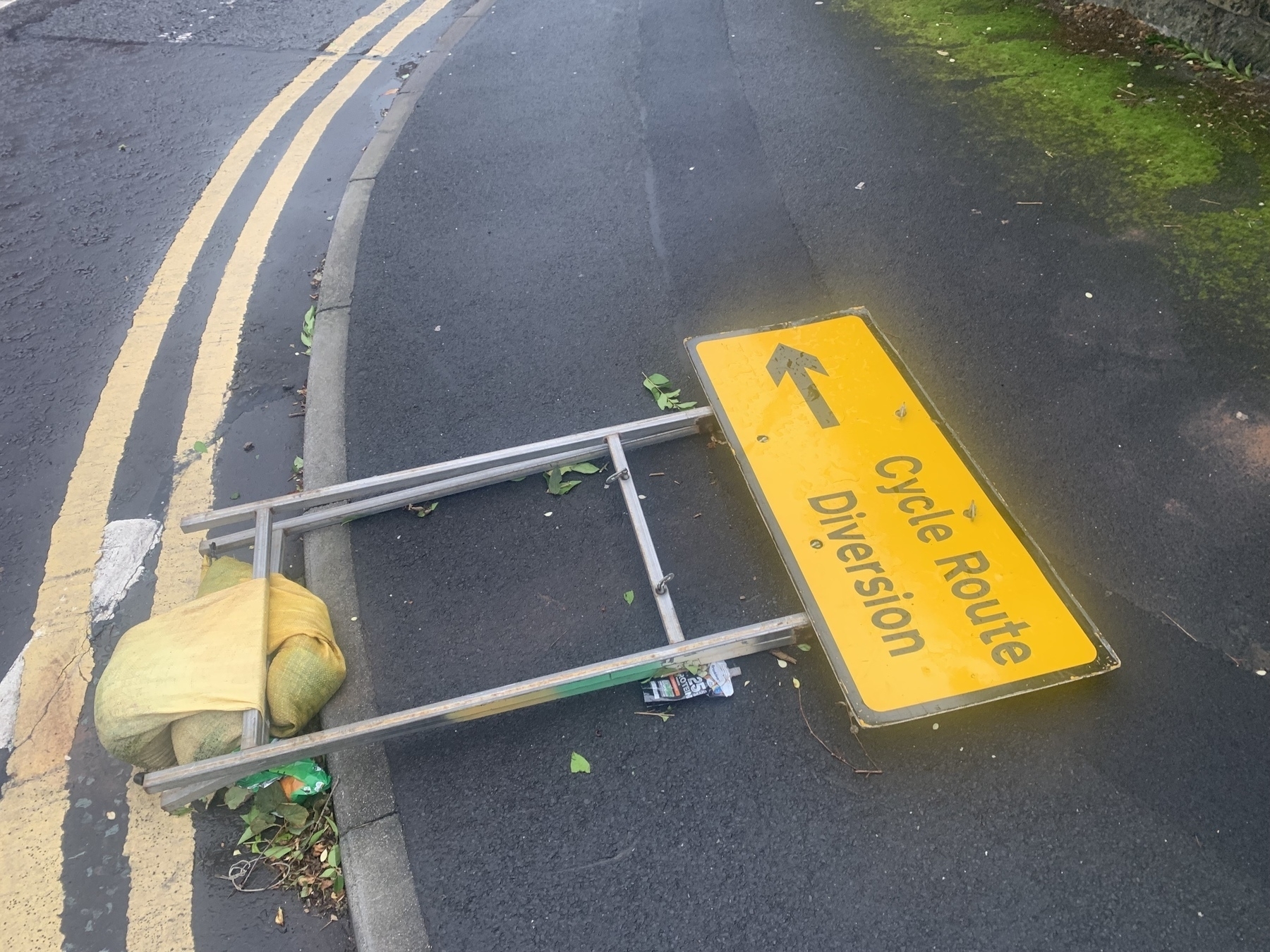 Yellow temporary road sign laying flat on the ground reading ‘Cycle Route Diversion’.