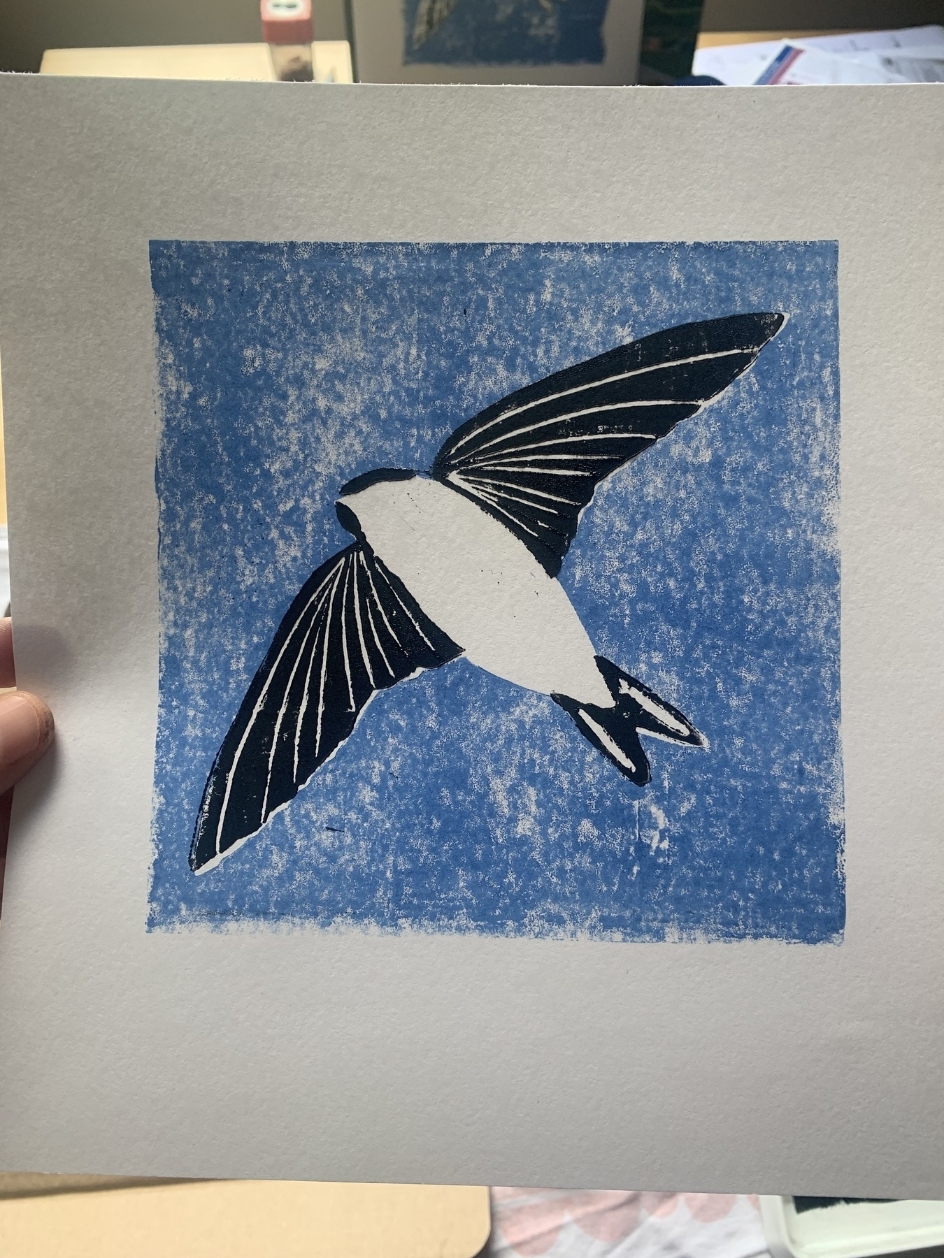 Two colour linocut print. Black and white outline of a house martin on a blue background.