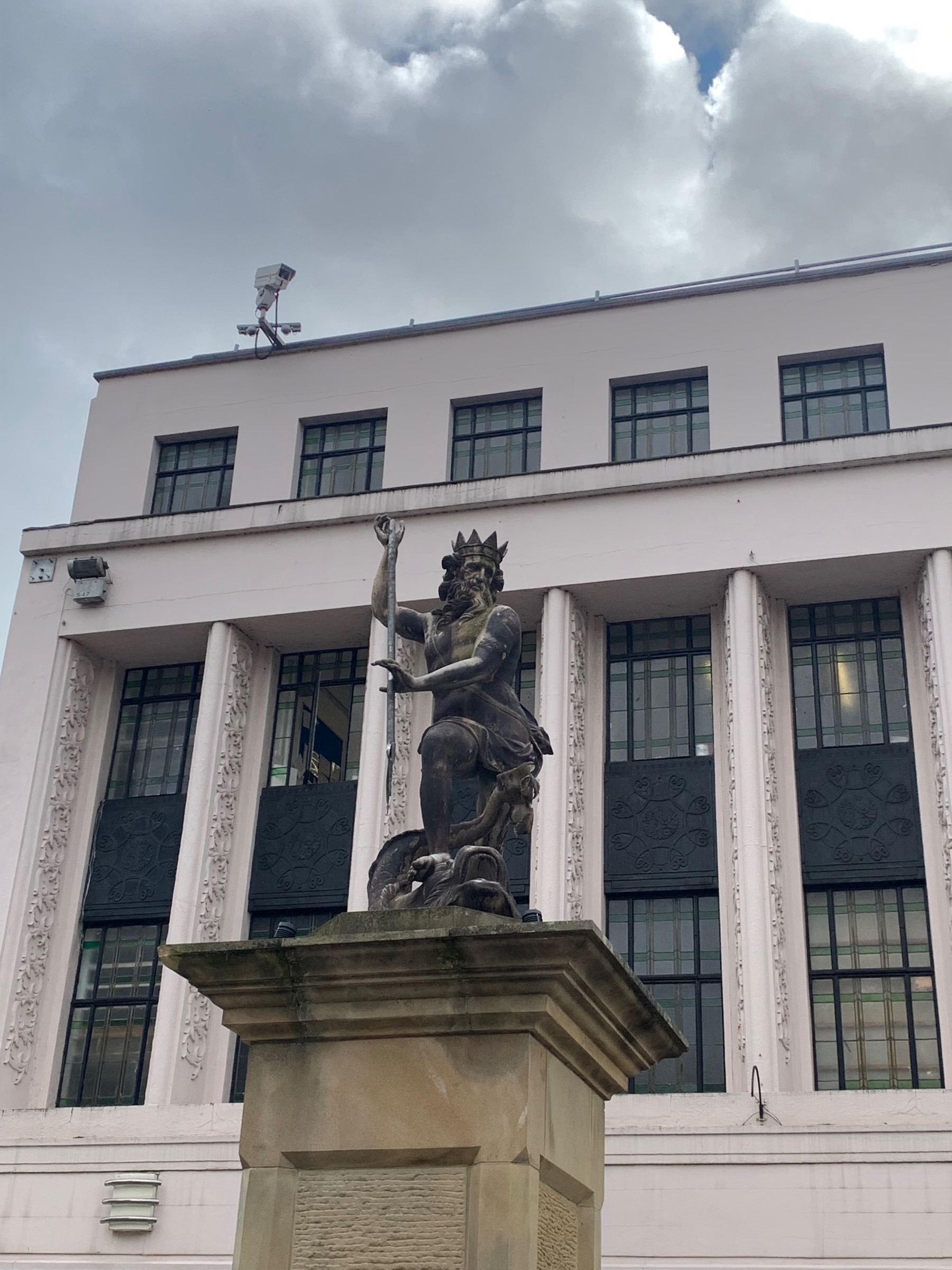 A statue of Neptune on a plinth in front of a decorative white building with lots of windows.