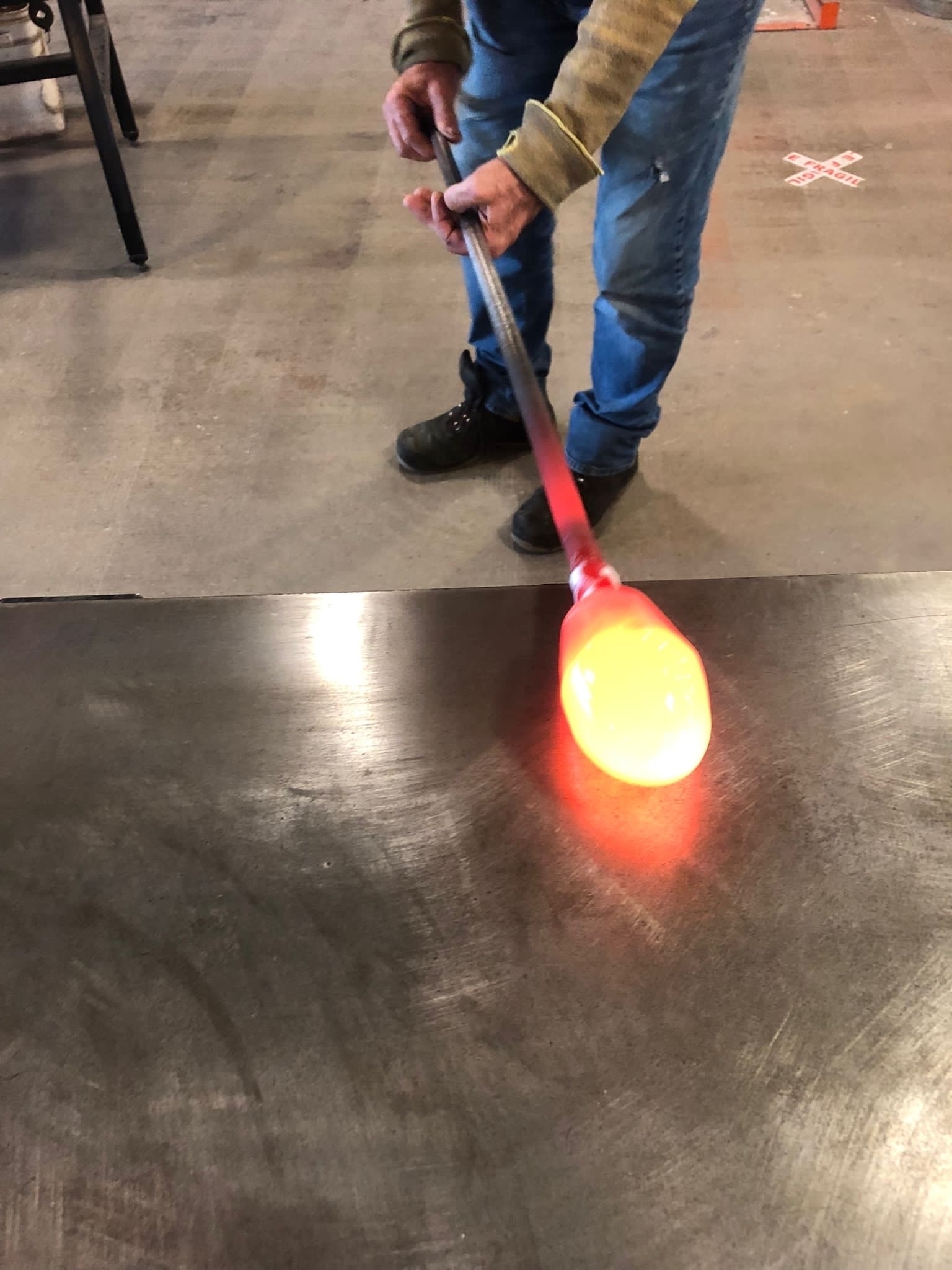 Molten glass on the end of a rod being worked on a metal counter top.